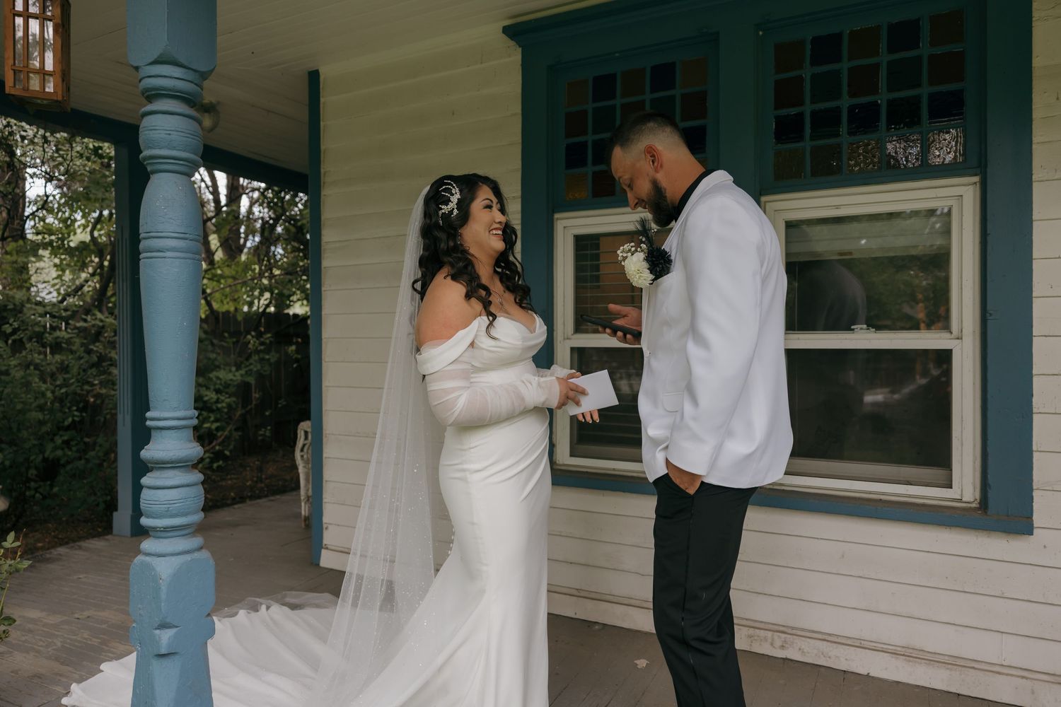 Bride and groom exchange vows on a charming porch, bride in elegant white gown with veil, groom in white shirt.