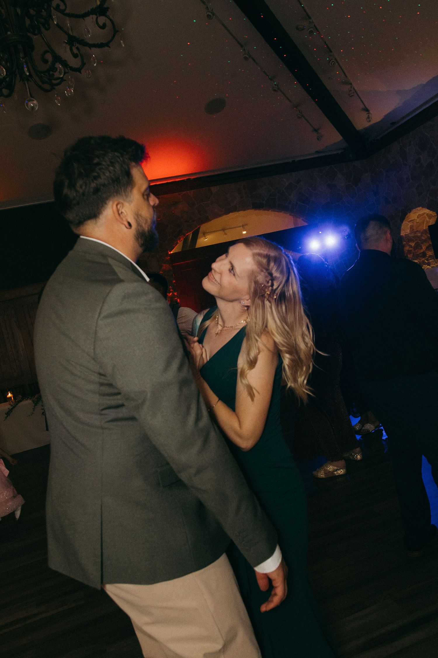 Couple sharing a romantic dance at a wedding reception, woman in green dress gazing up at partner under dim lights.