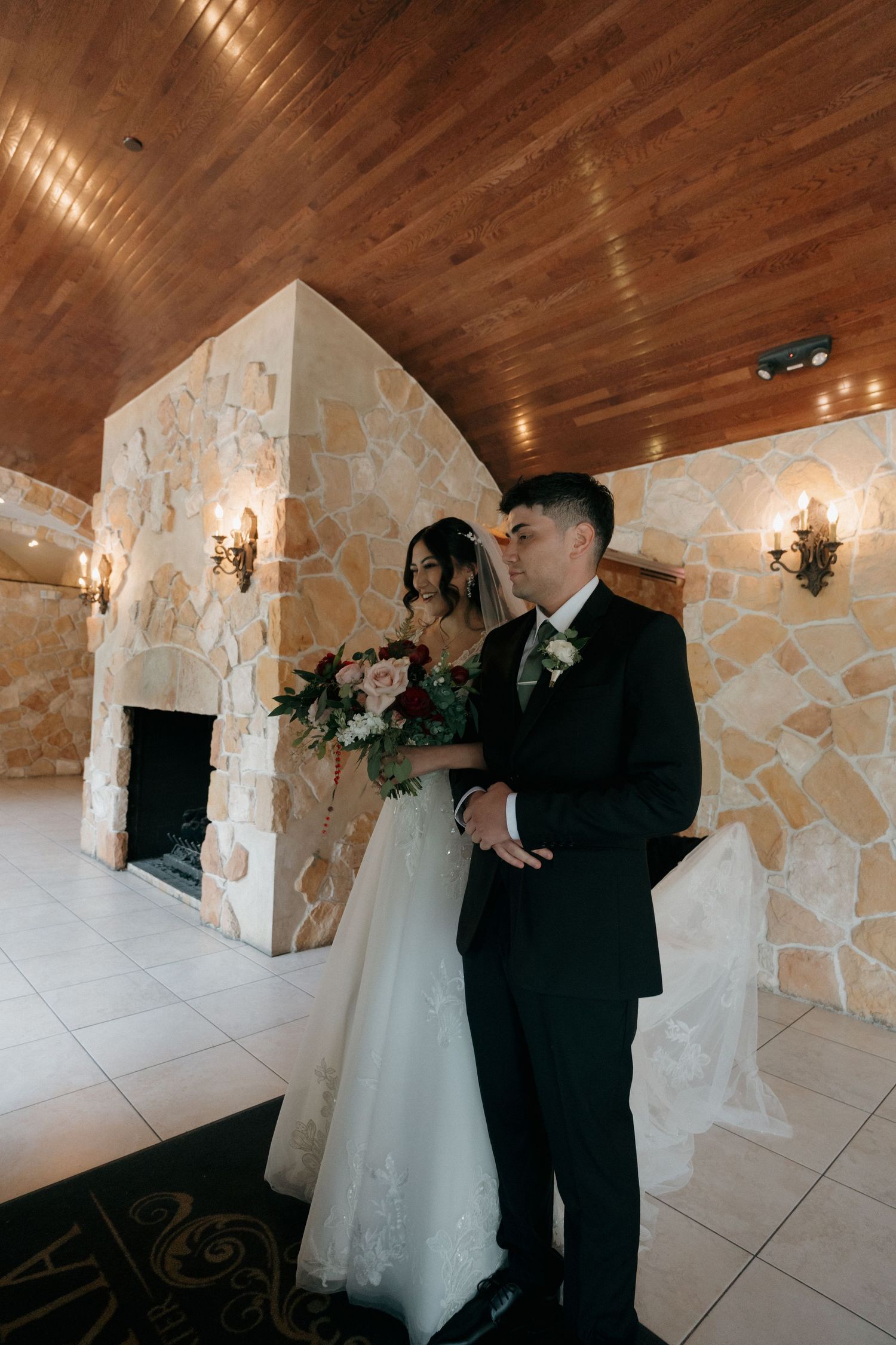 Bride and groom sharing romantic moment by stone fireplace in wedding venue interior.