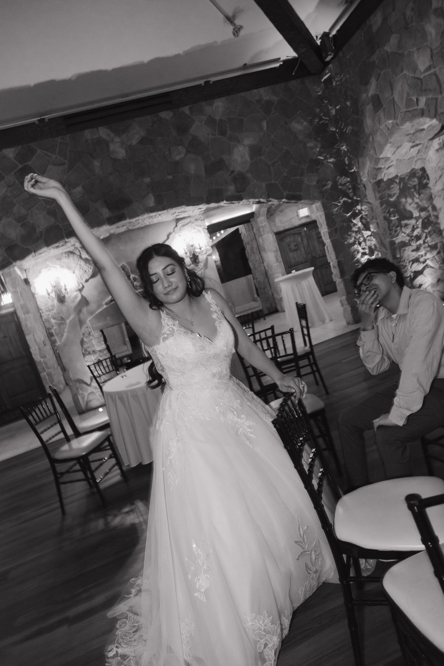 Bride in lace gown twirls with arm raised on the dance floor at her wedding reception.