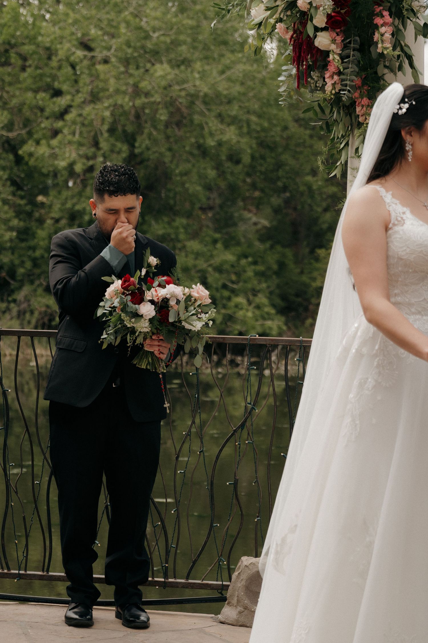 Emotional groom holds bridal bouquet and covers his mouth as bride approaches the altar.