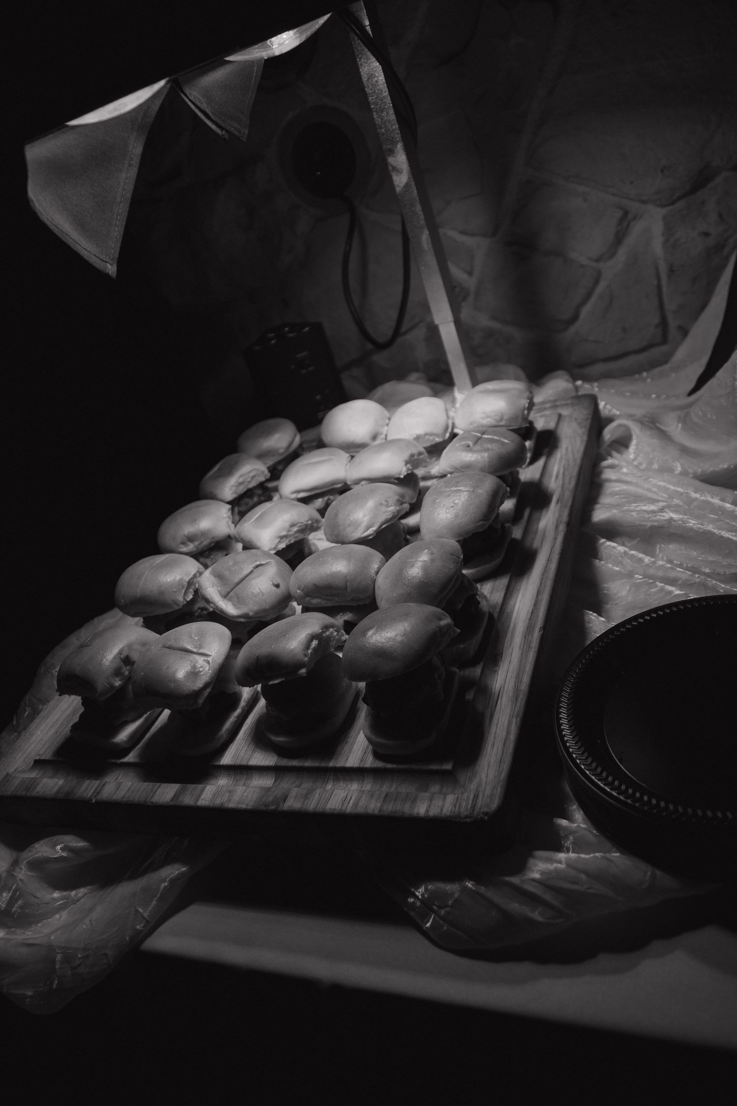Elegant display of small round pastries on wooden board under spotlight at wedding reception.