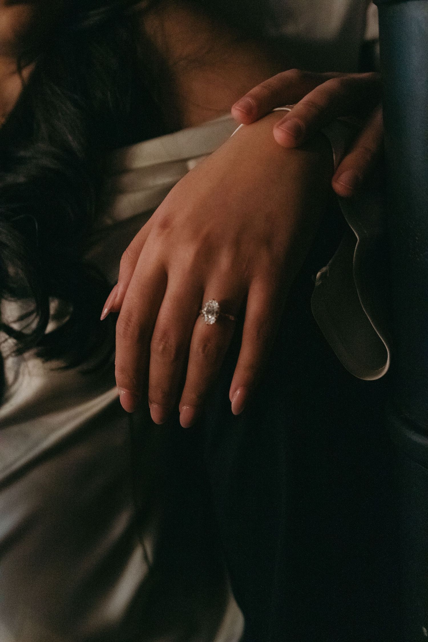 Close-up shot of hands with an engagement ring in moody lighting.