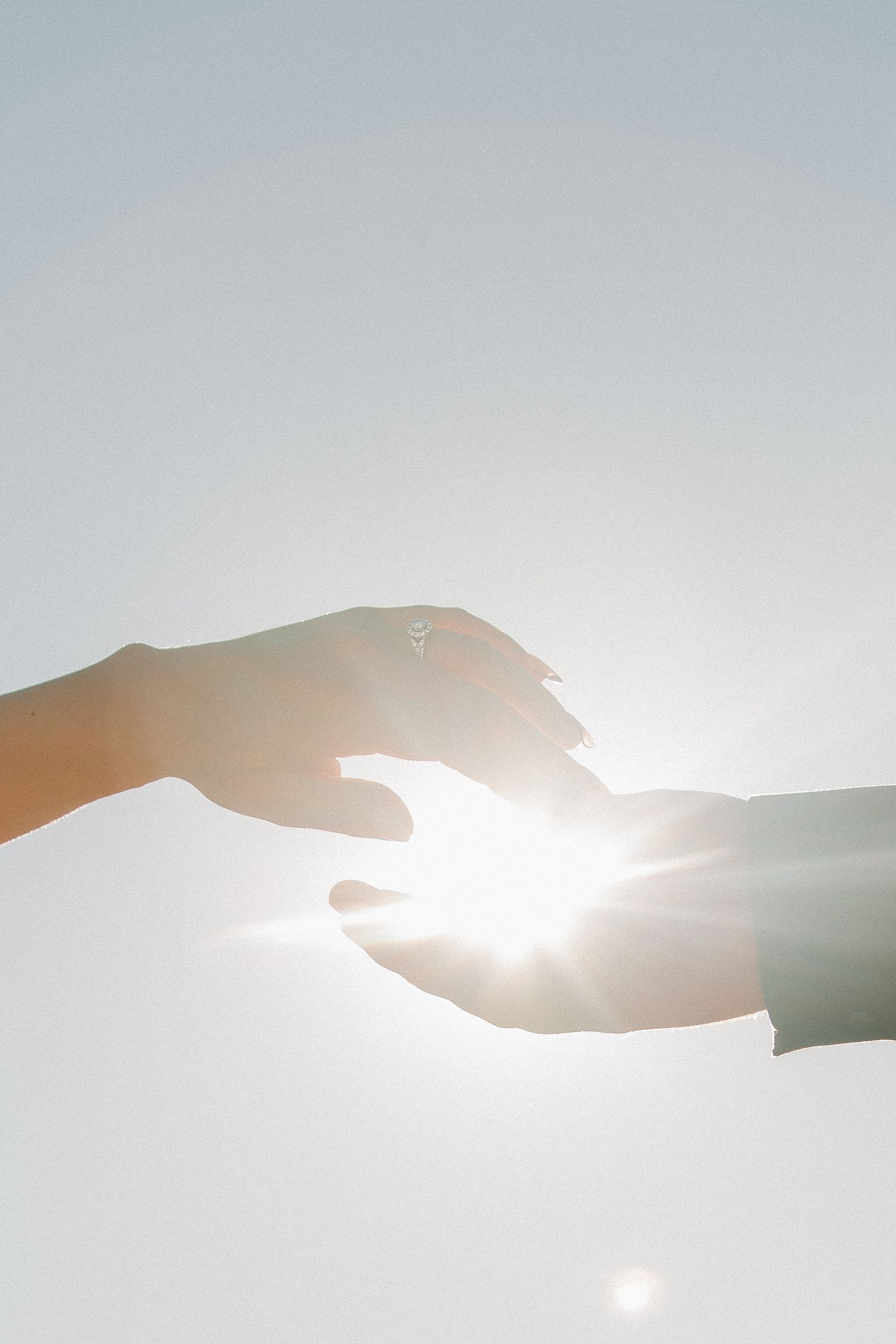 Two silhouetted hands reaching towards each other with bright sunlight glowing between them in a minimalist composition.