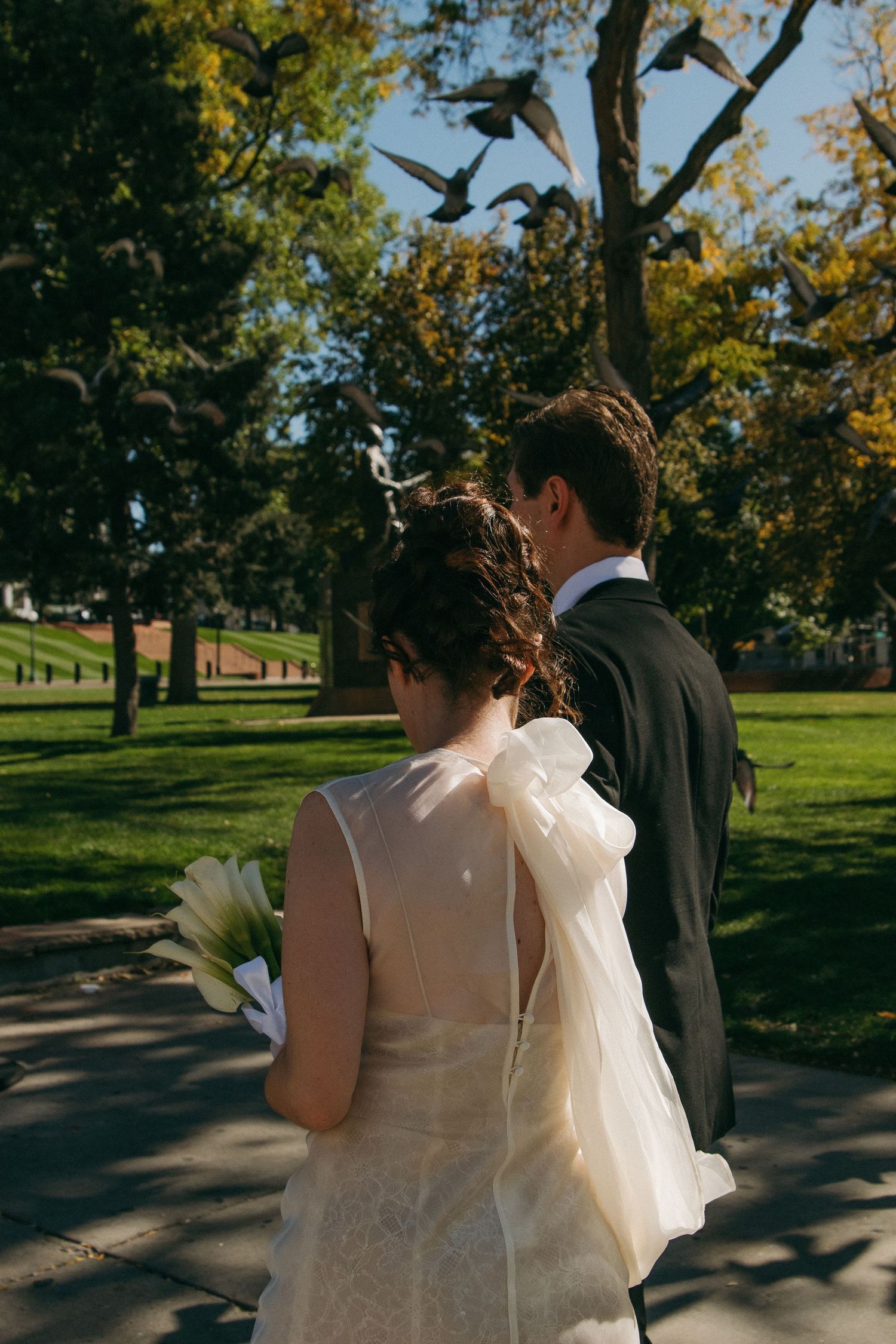 Couple walking through a sunny park with autumn trees on a wedding day.
