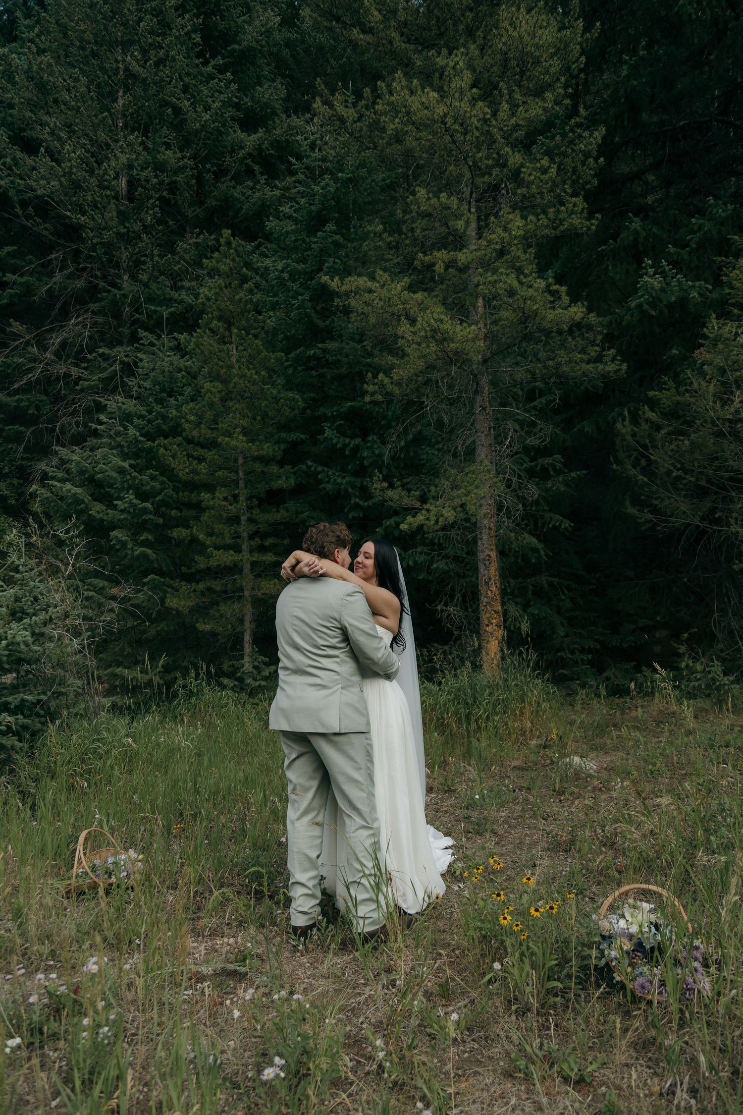 Newlywed couple shares a warm embrace in a forest meadow surrounded by wildflowers after their elopement.