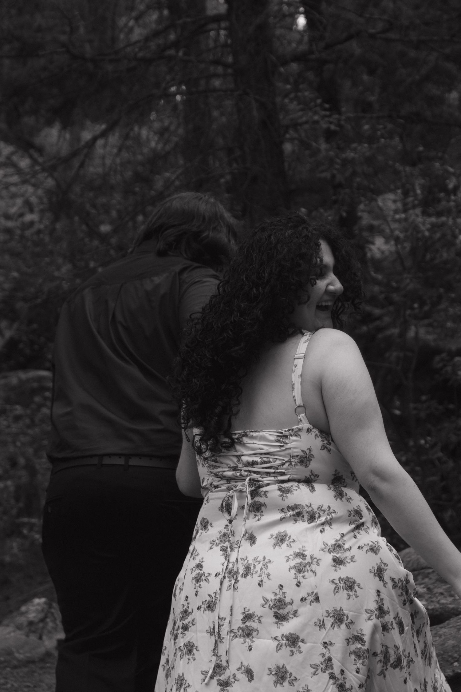 A couple in a woodland setting wearing contrasting outfits of black and floral.