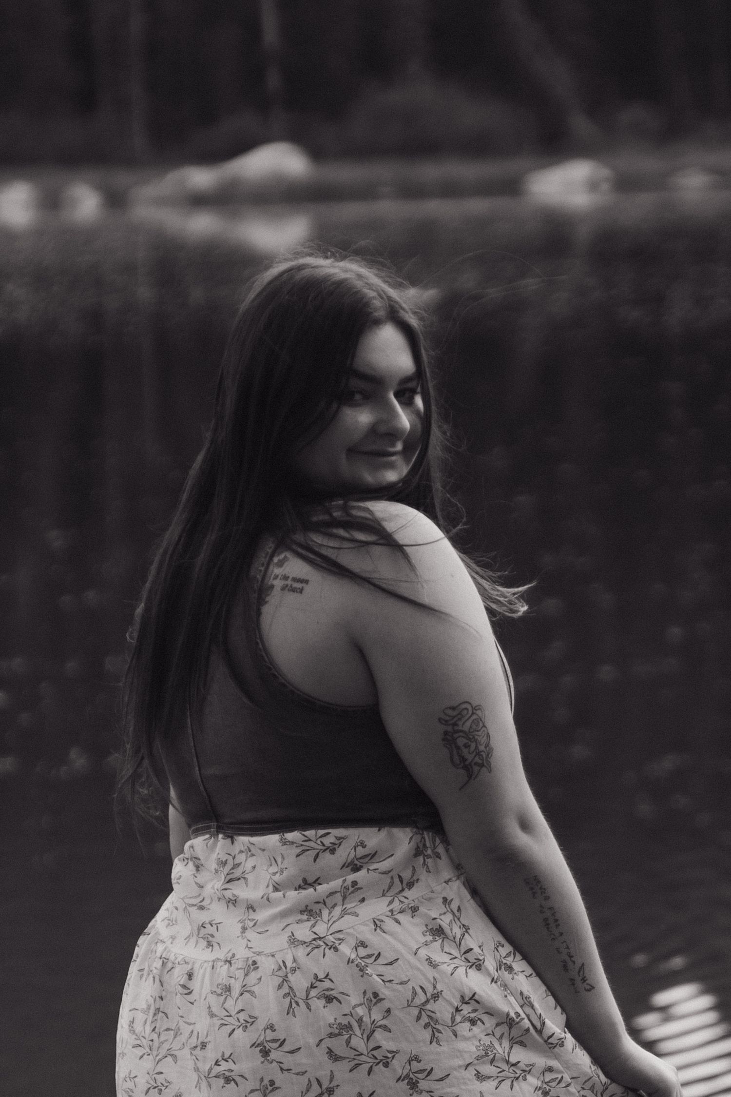 Black and white portrait series of a person in a floral dress posing by a lake in a natural outdoor setting.