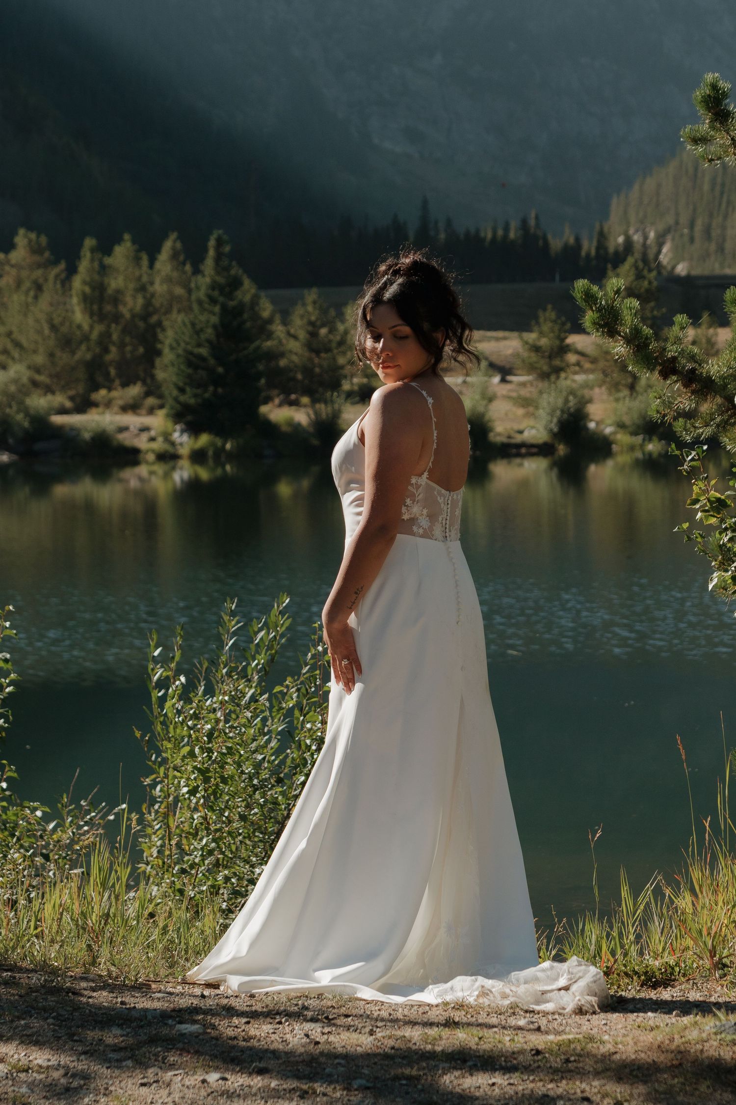 A white wedding dress flows elegantly against a scenic mountain lake backdrop.