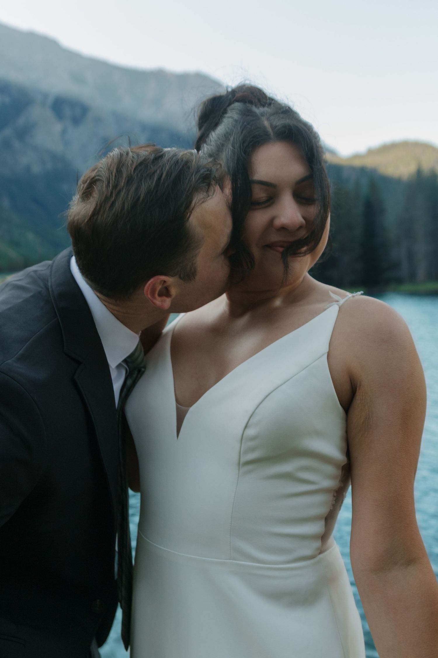 Tender moment between newlyweds against stunning mountain lake backdrop.