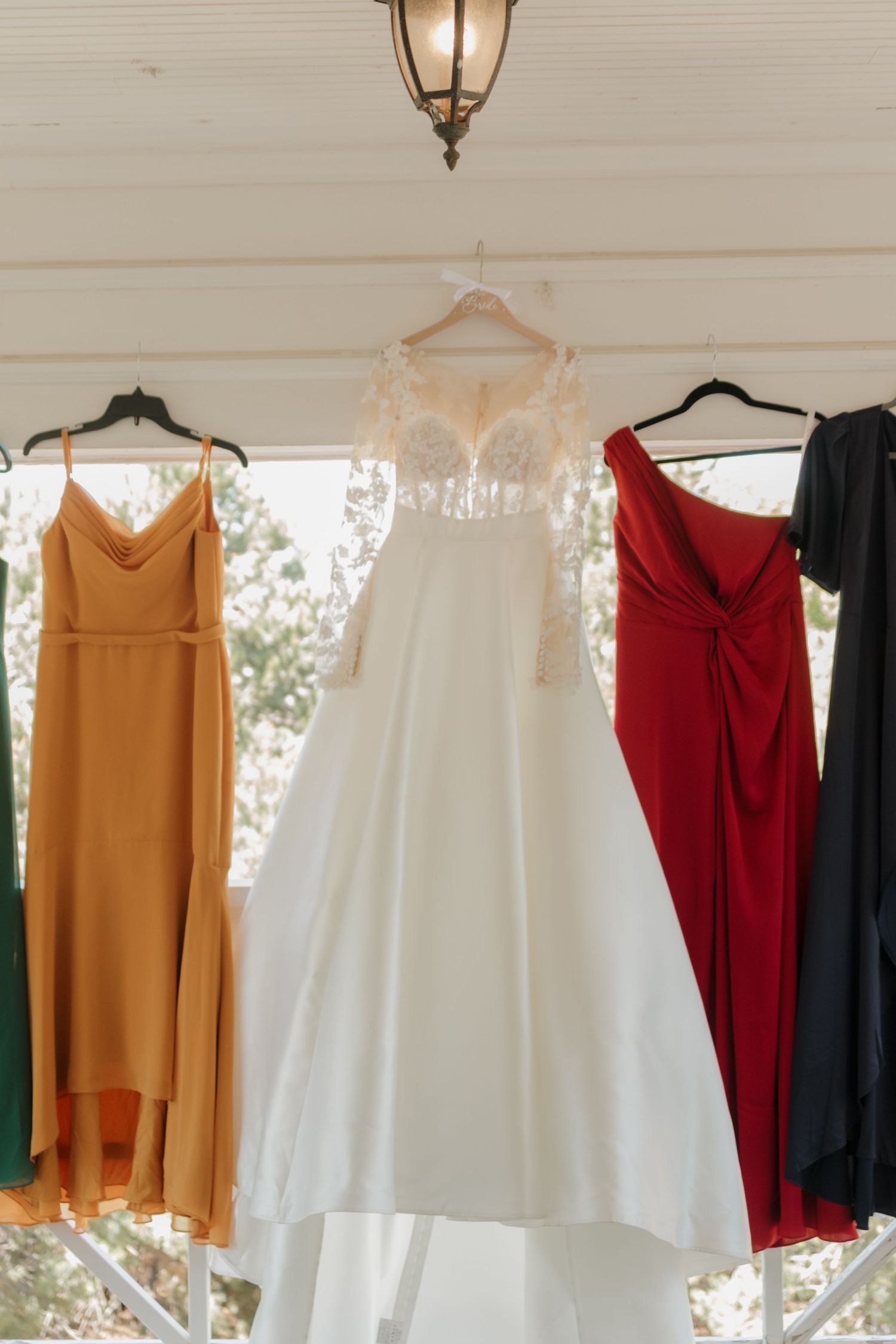 Wedding dresses and colorful bridesmaid gowns hanging on a rack against a white wall.