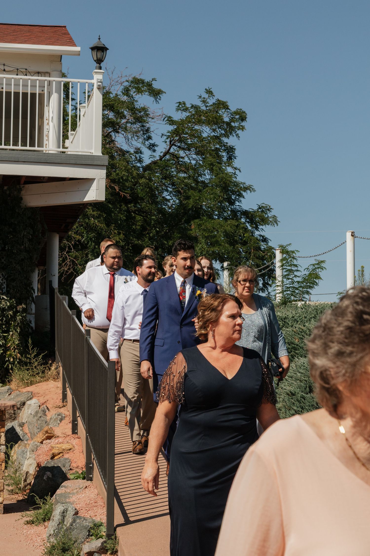 Wedding party and guests walking along an outdoor path with mountain views.