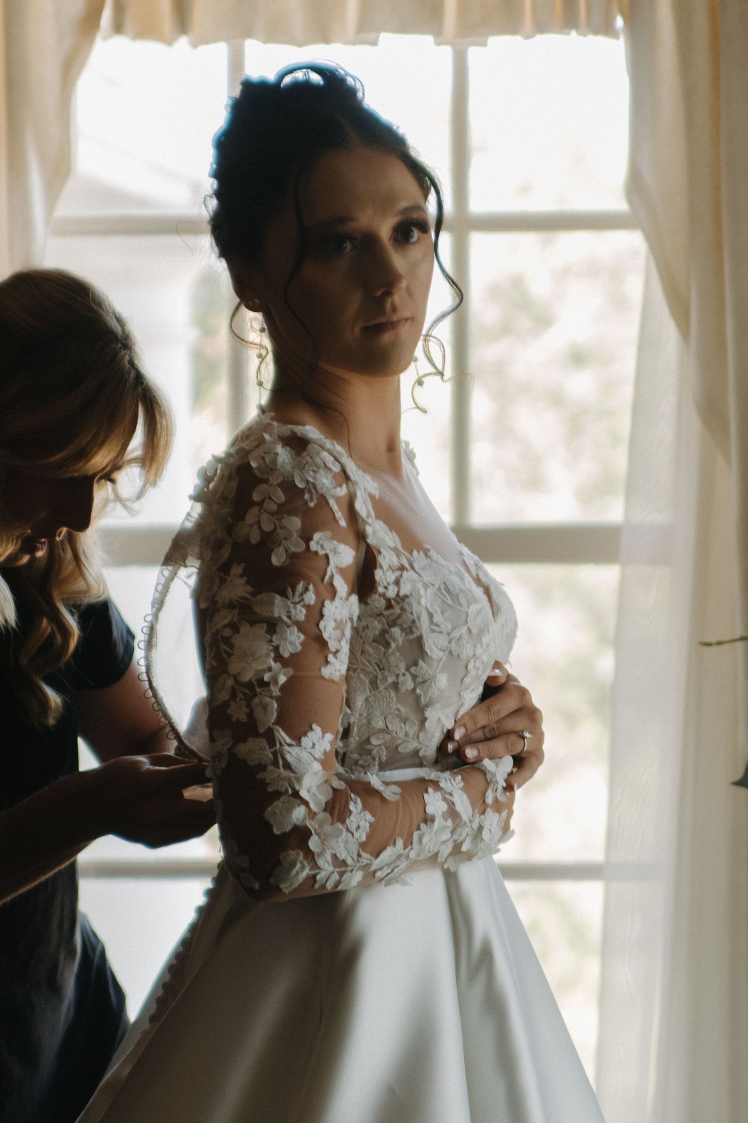 Wedding gown with delicate lace sleeves and floral details being adjusted in natural light.