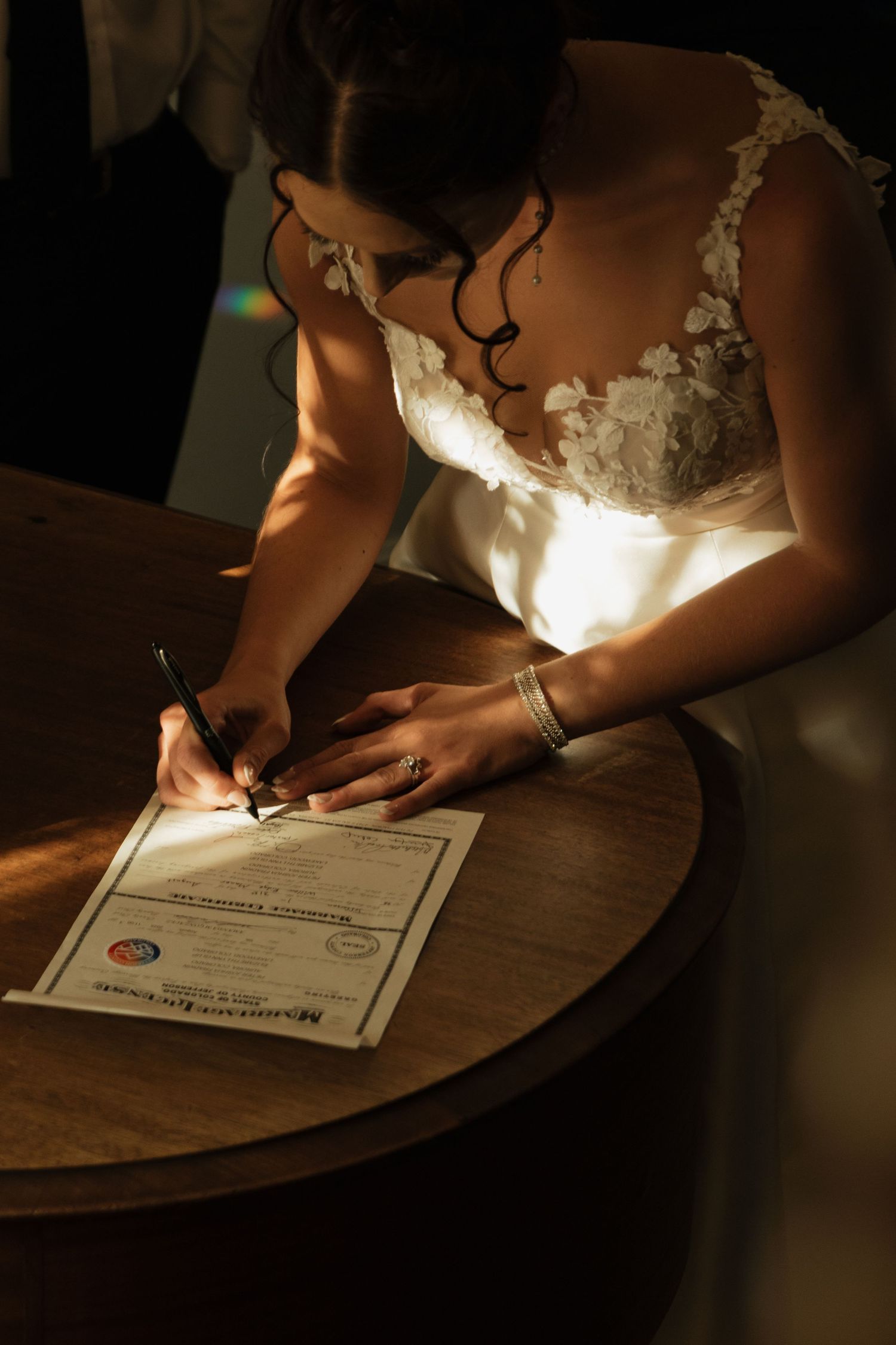 Signing of wedding documents in dramatic lighting on wooden surface.