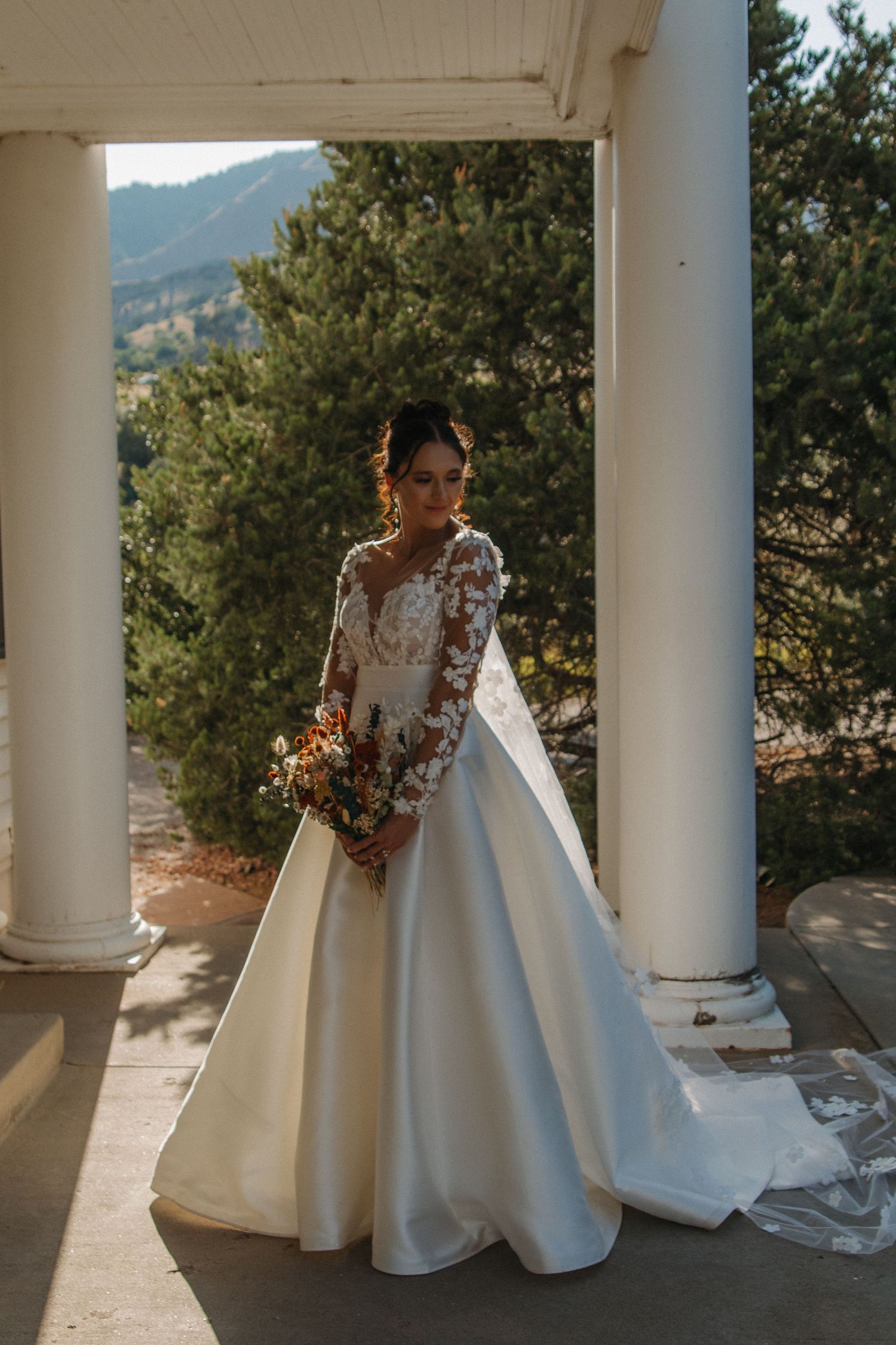 Elegant bridal portraits on columned porch with mountain scenery in background.