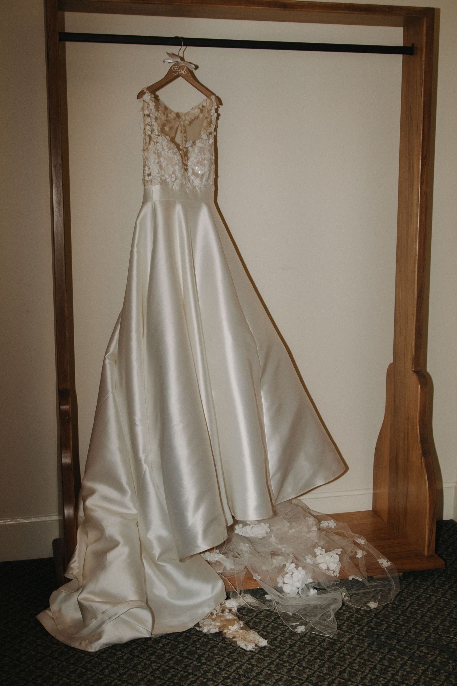 White wedding dress displayed on hanger against dark wooden wall.