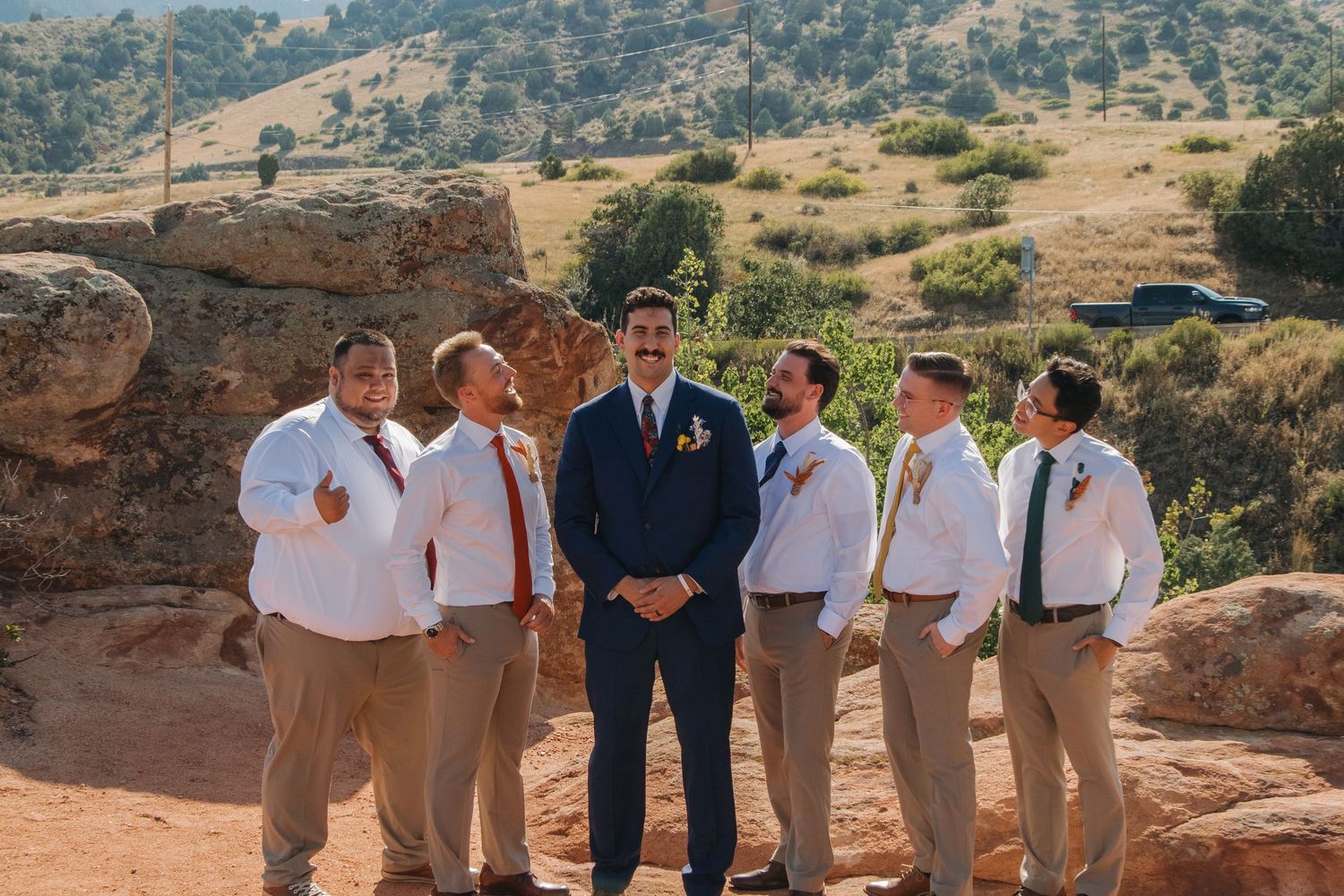 Wedding party in mix of navy and khaki attire poses against desert mountain backdrop.