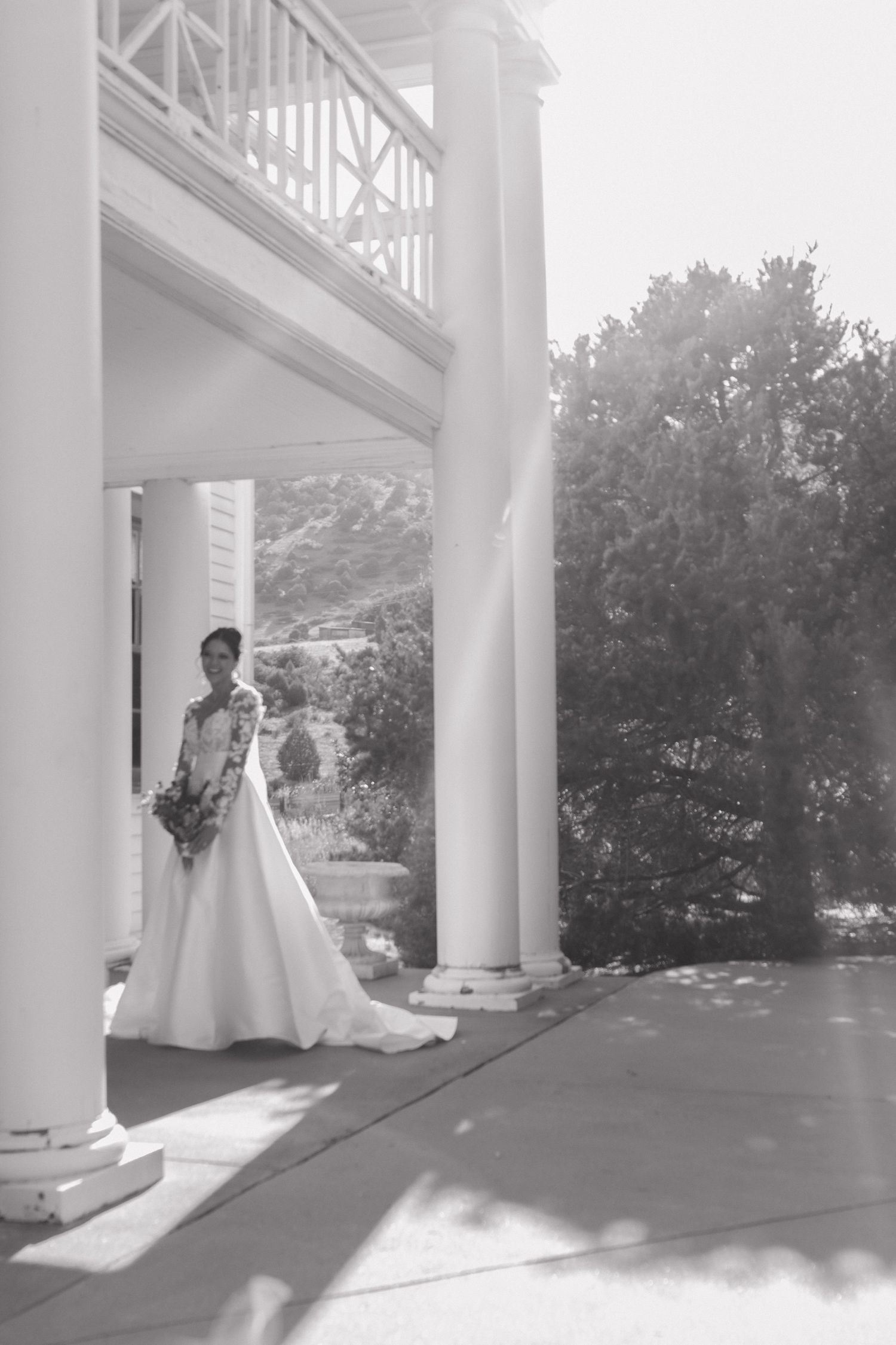 Wedding photos taken under a white columned porch with natural lighting streaming in.