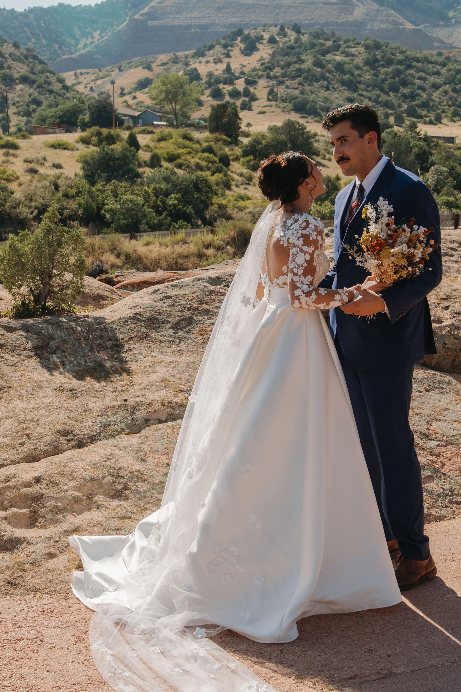 Couple in wedding attire posing against dramatic mountain landscape.