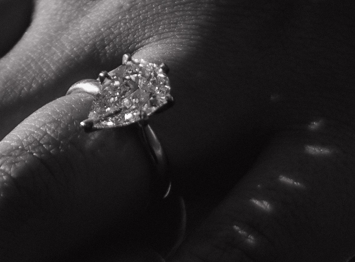 Black and white close-up of a stunning pear-shaped diamond solitaire engagement ring on a finger.