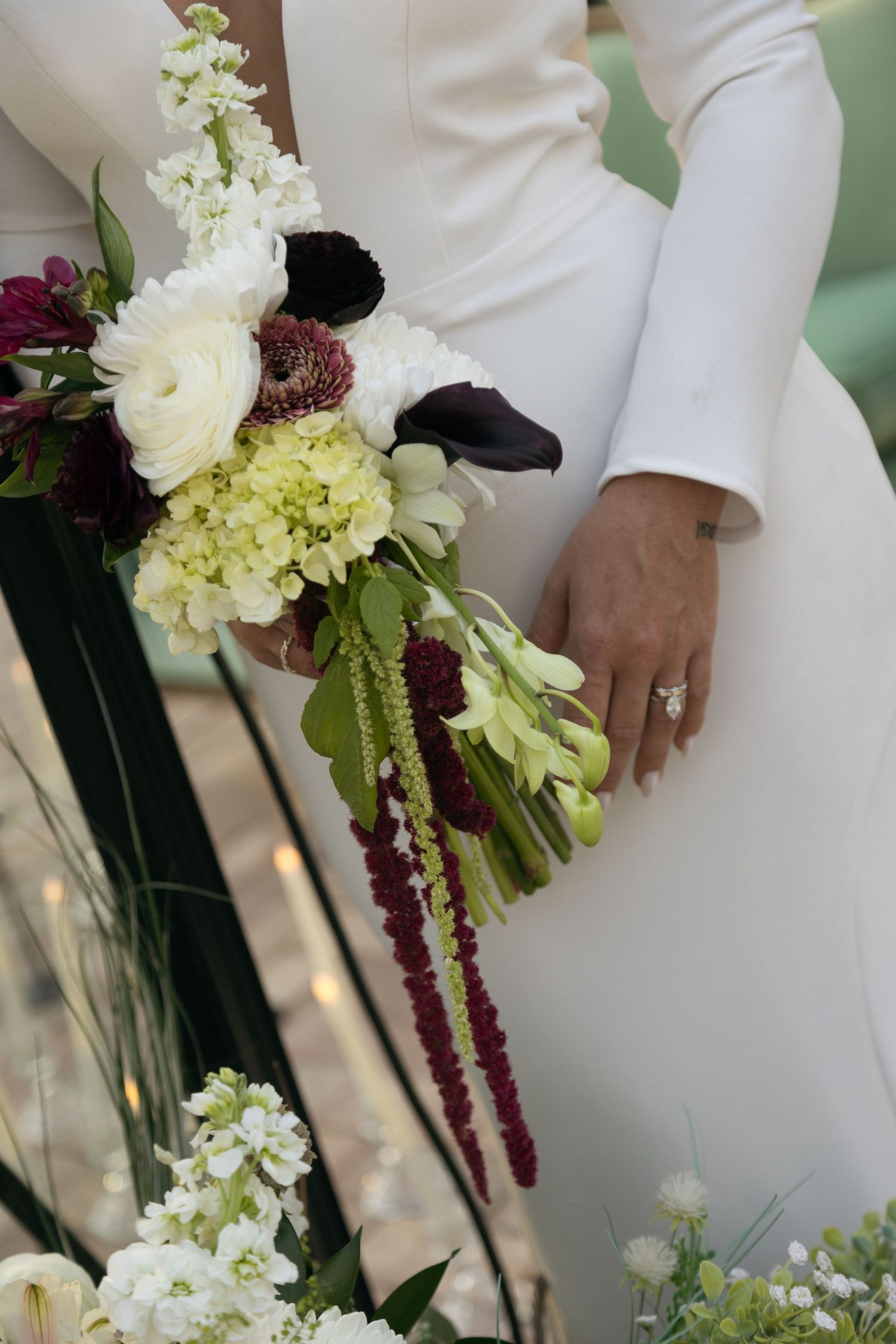 Close-up of bride holding cascading bouquet with white ranunculus, dark calla lilies, and burgundy amaranthus.