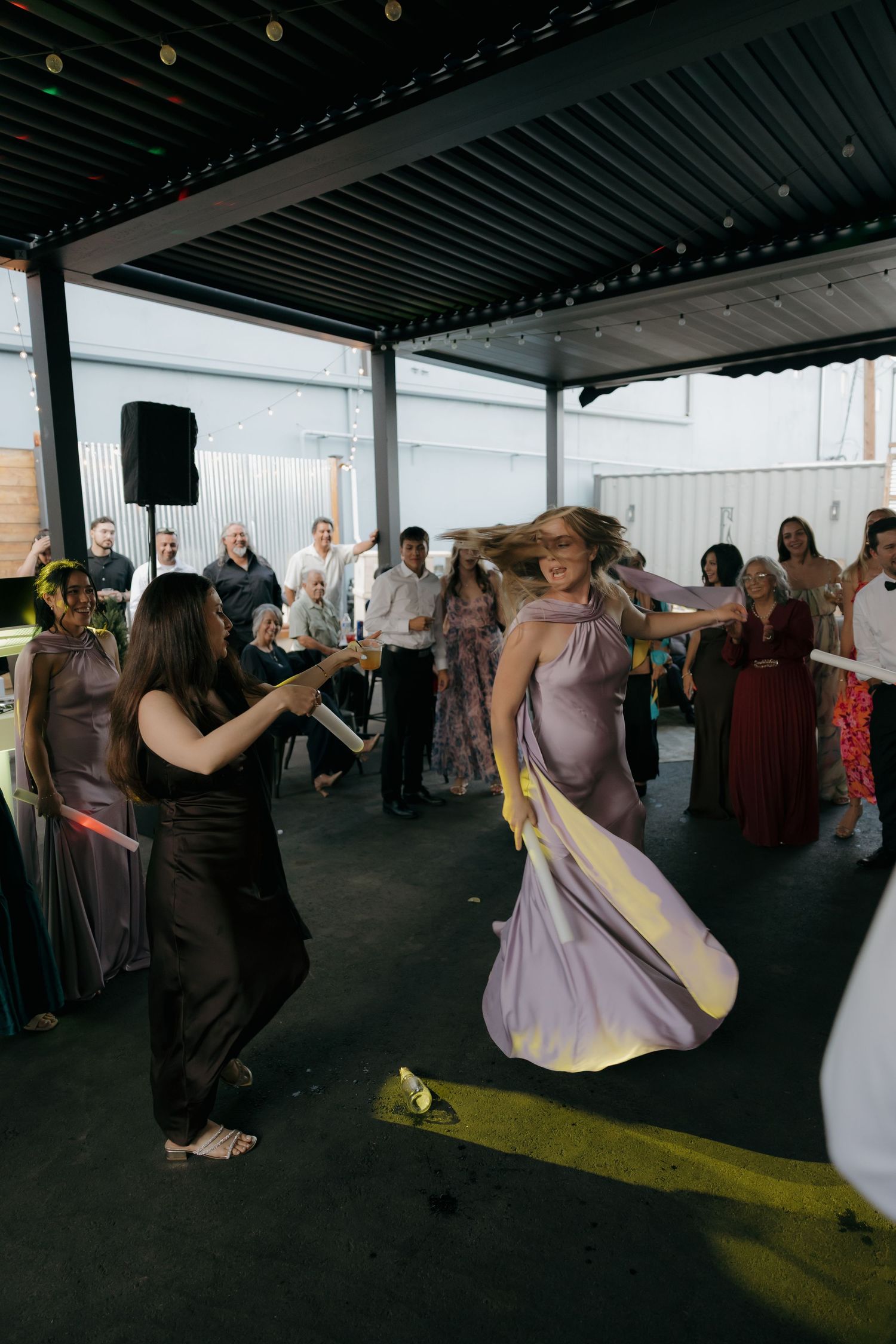 Guests dancing at outdoor wedding reception under pergola, woman spinning in purple bridesmaid dress.