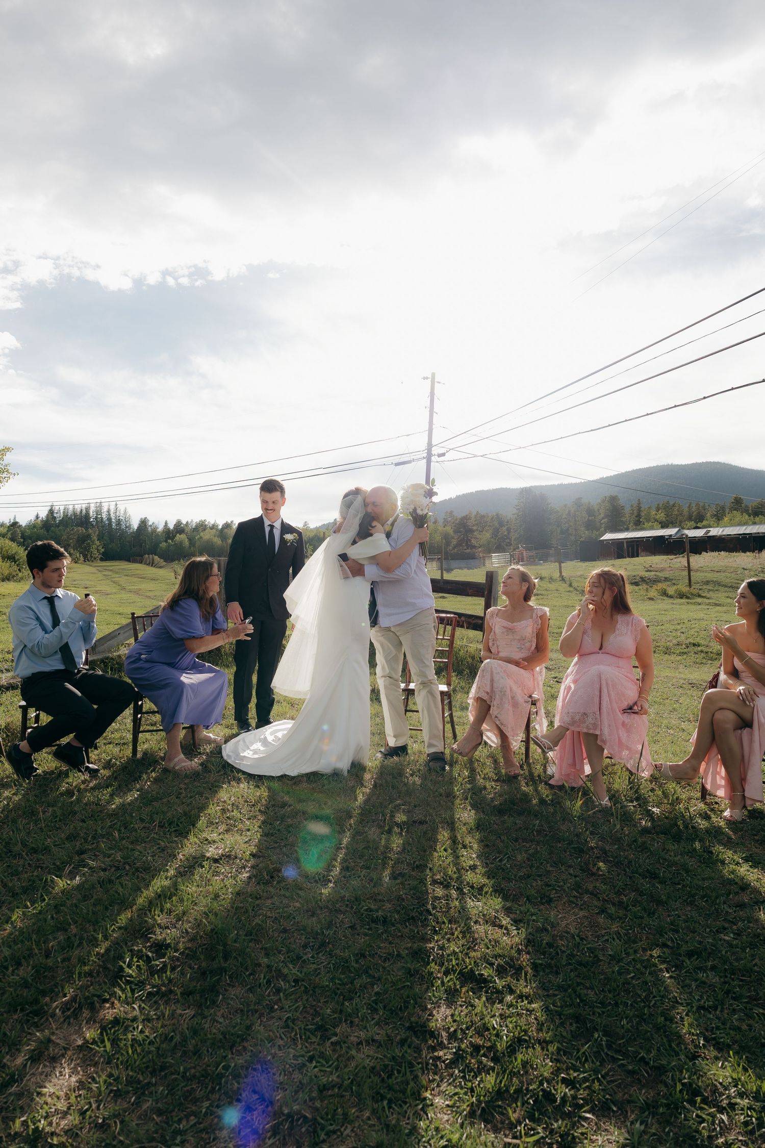 Bride embracing a guest during intimate outdoor wedding ceremony with mountain views.