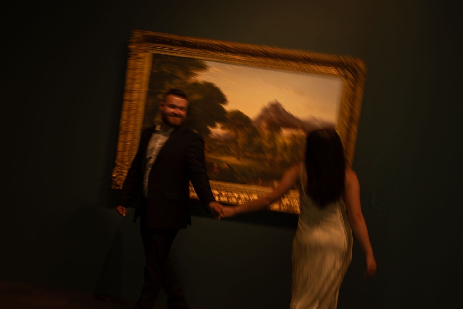 Romantic couple embraces in a dimly lit art gallery with paintings visible in the background.
