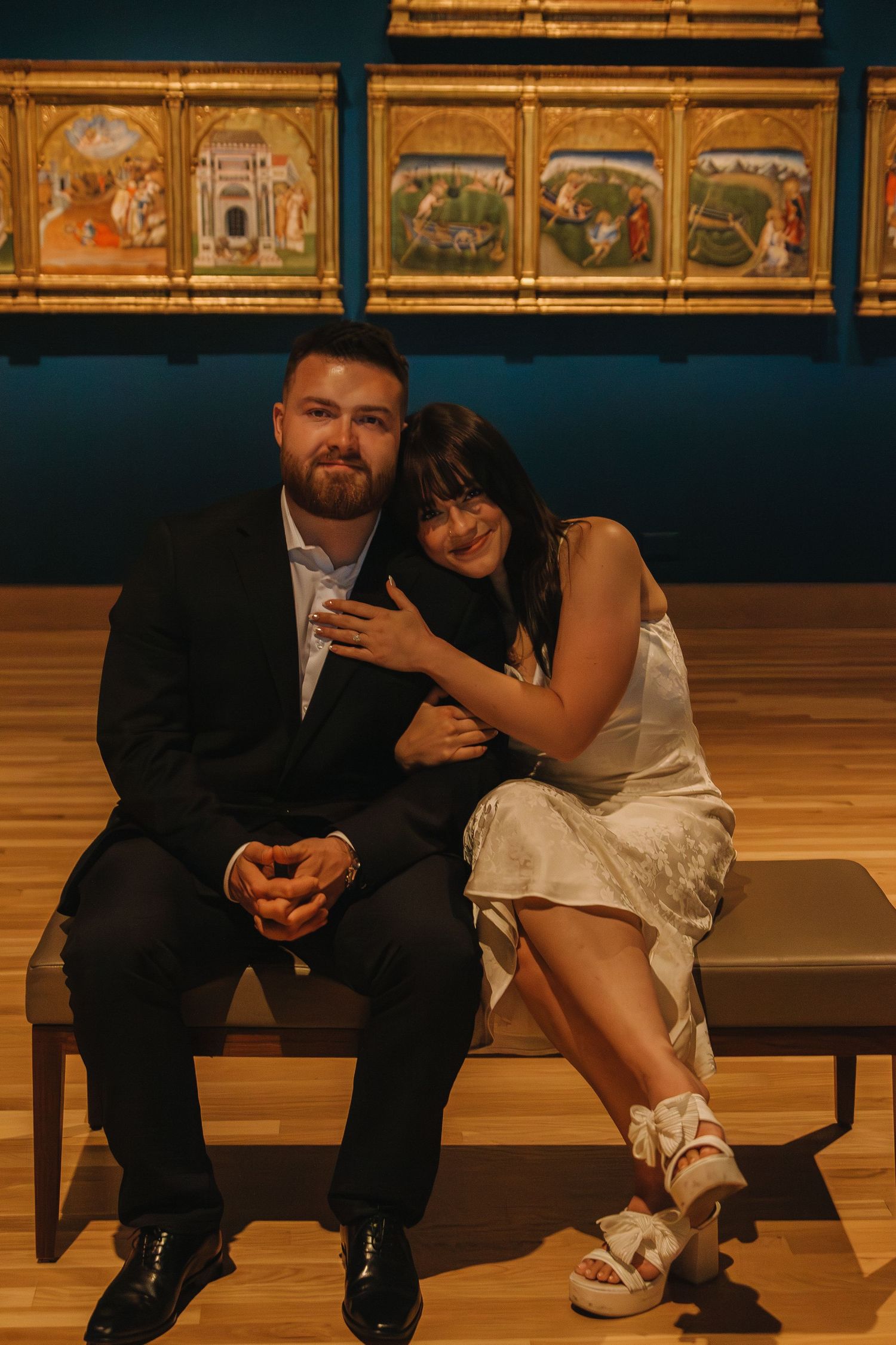 Couple sitting on museum bench with art gallery paintings visible in the background.