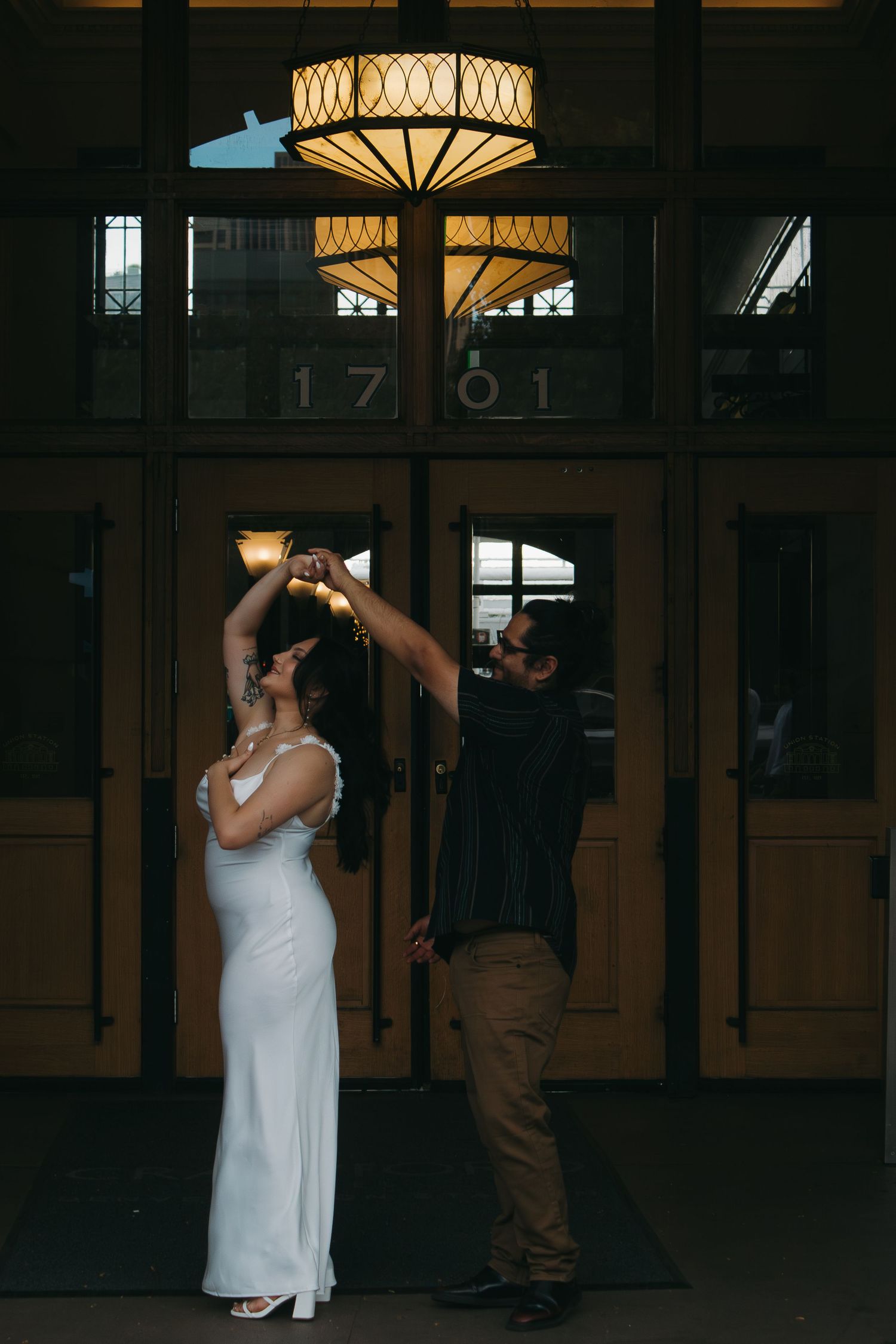 A romantic evening dance captured in a dimly lit venue with decorative lighting overhead.