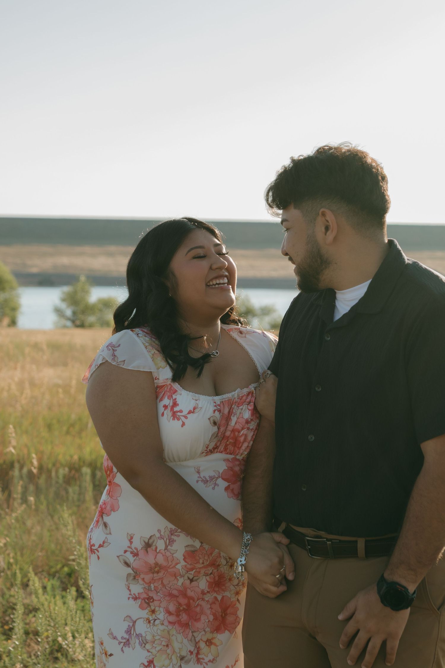 Playful couple laughing together in an outdoor photoshoot against golden meadow backdrop.