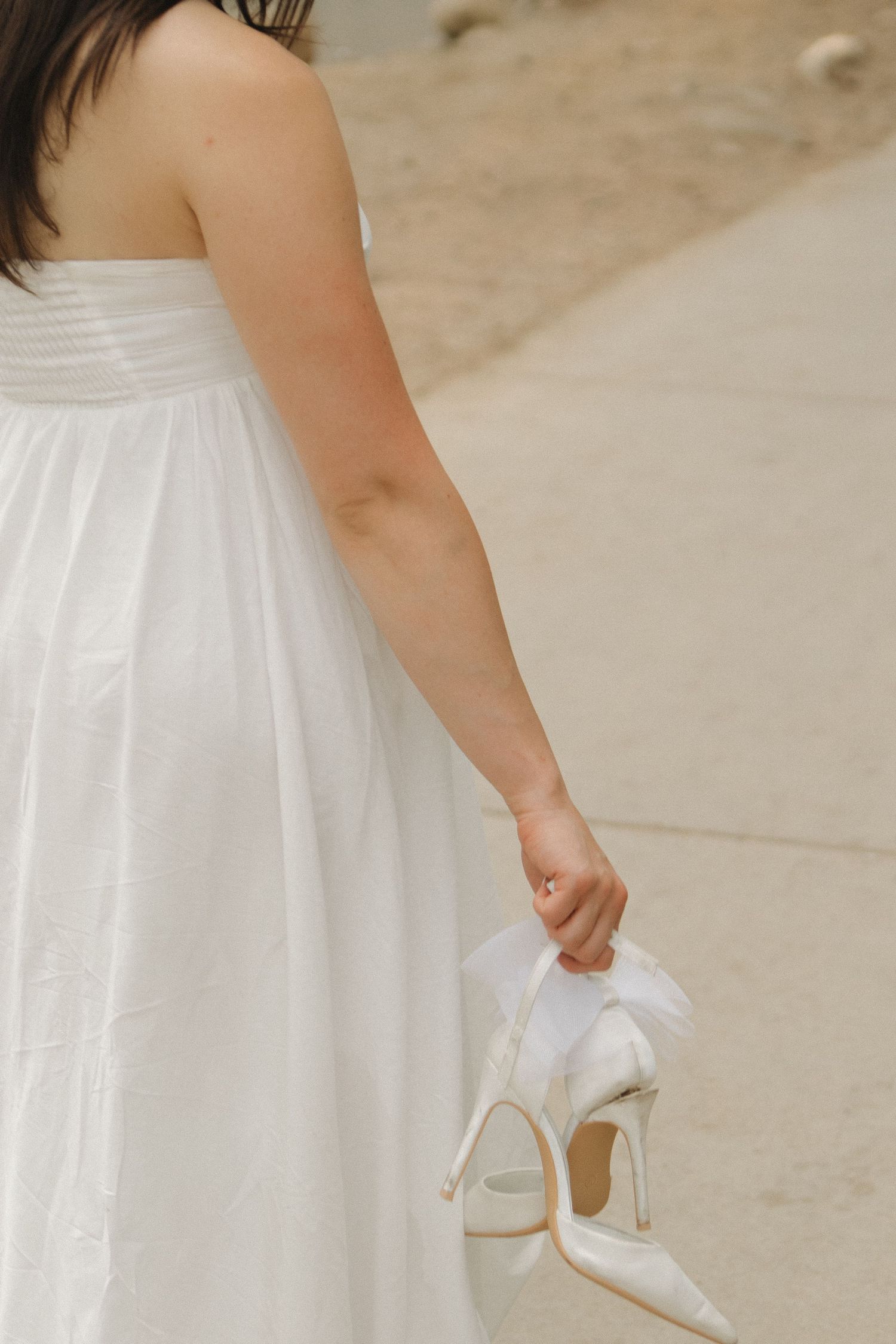 A flowing white bridal dress photographed in close-up details with matching white heels.