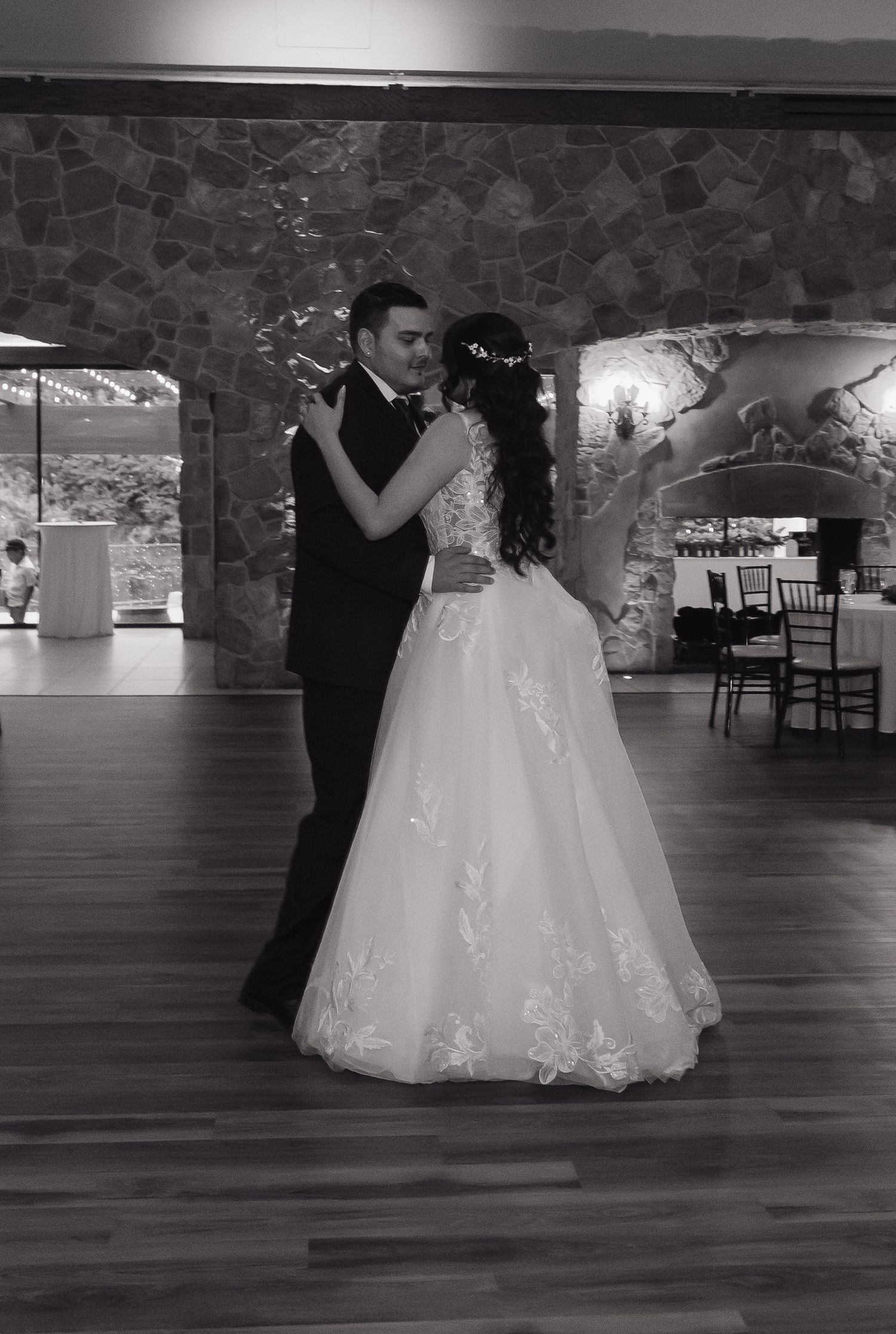Bride and groom share their first dance in a black and white photo at a rustic stone wedding venue.