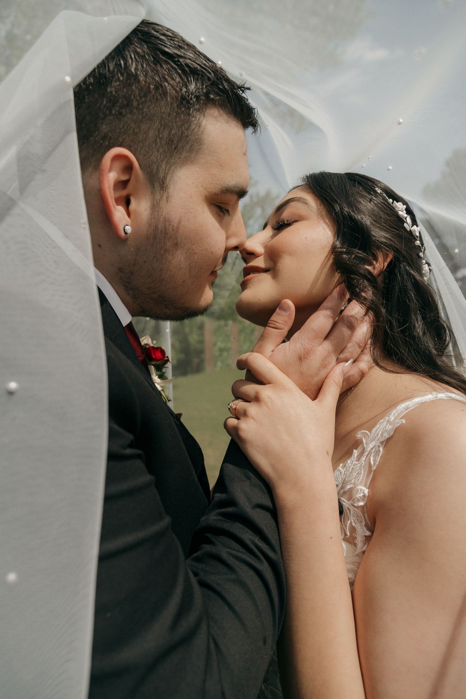 Intimate close-up of bride and groom almost kissing under a veil, groom gently holding bride's face.