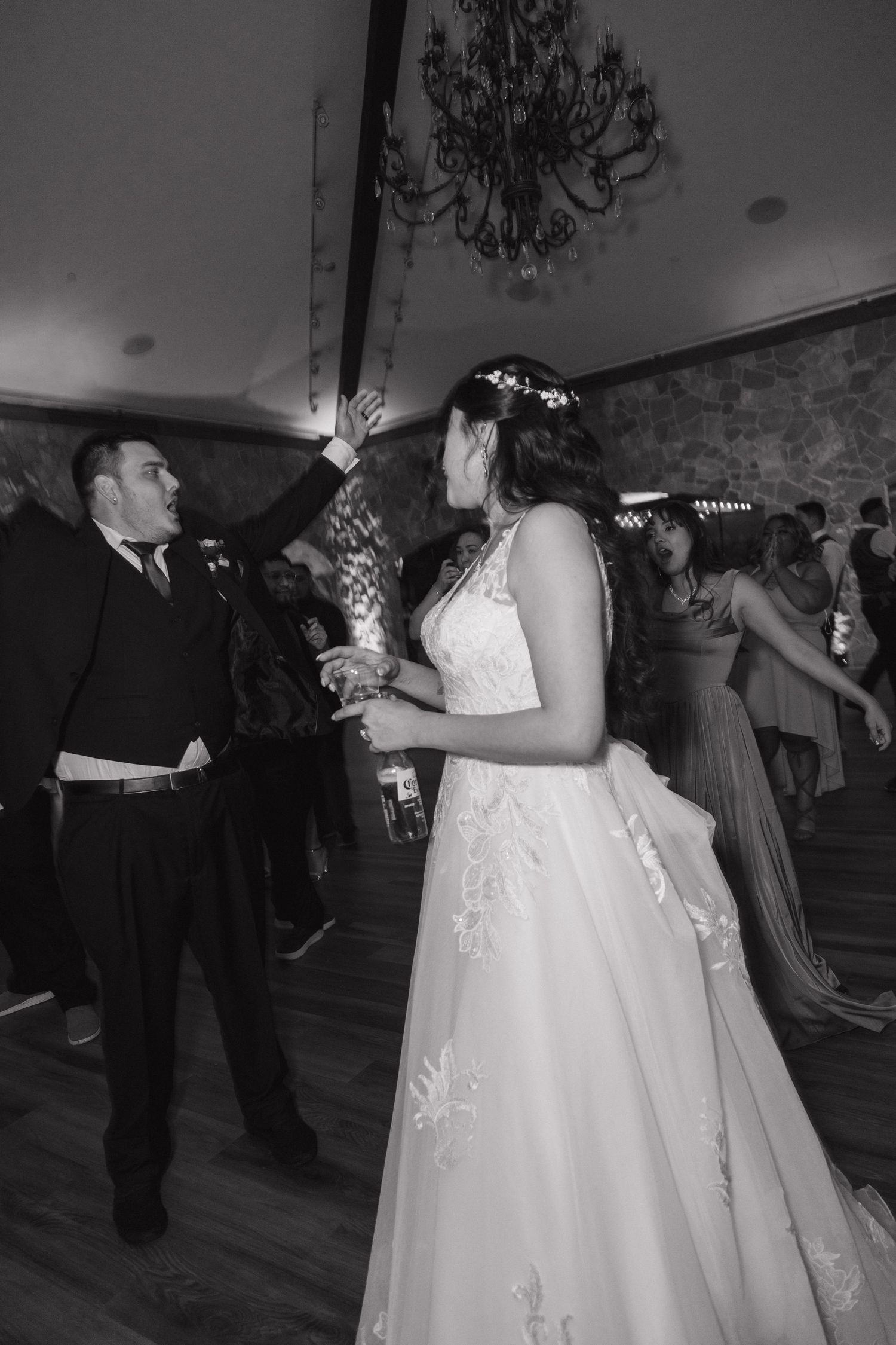 Black and white photo of bride and groom sharing a first dance surrounded by guests at their wedding.