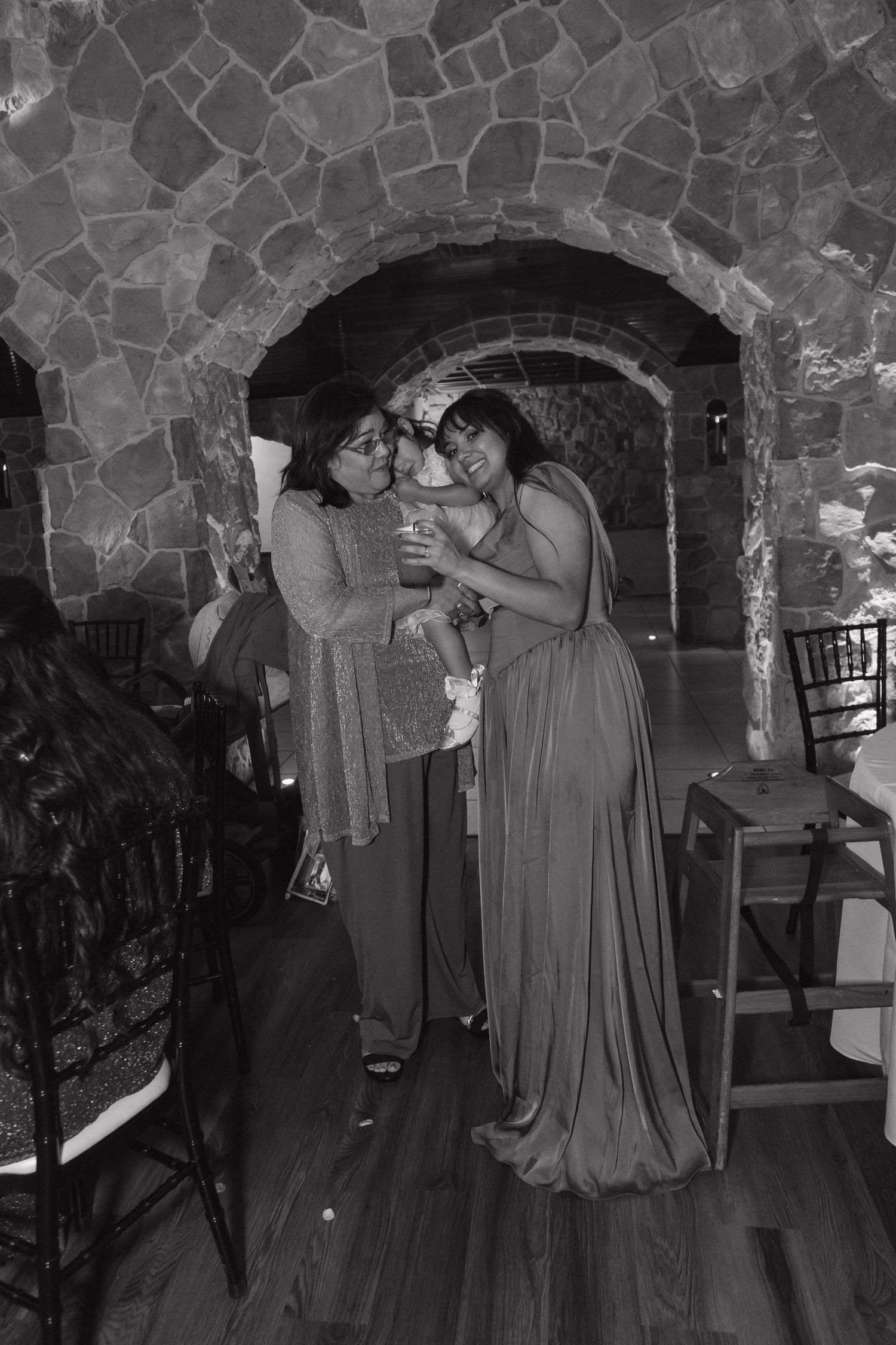 Black and white photo of women embracing and smiling in stone arch wedding venue.