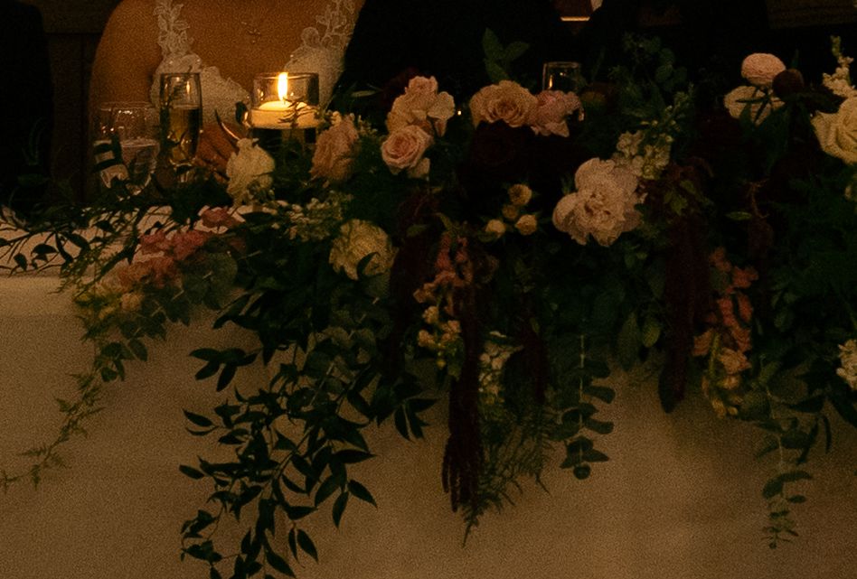 Elegant wedding table arrangement with white roses, greenery, and candlelight in a romantic dimly lit setting.