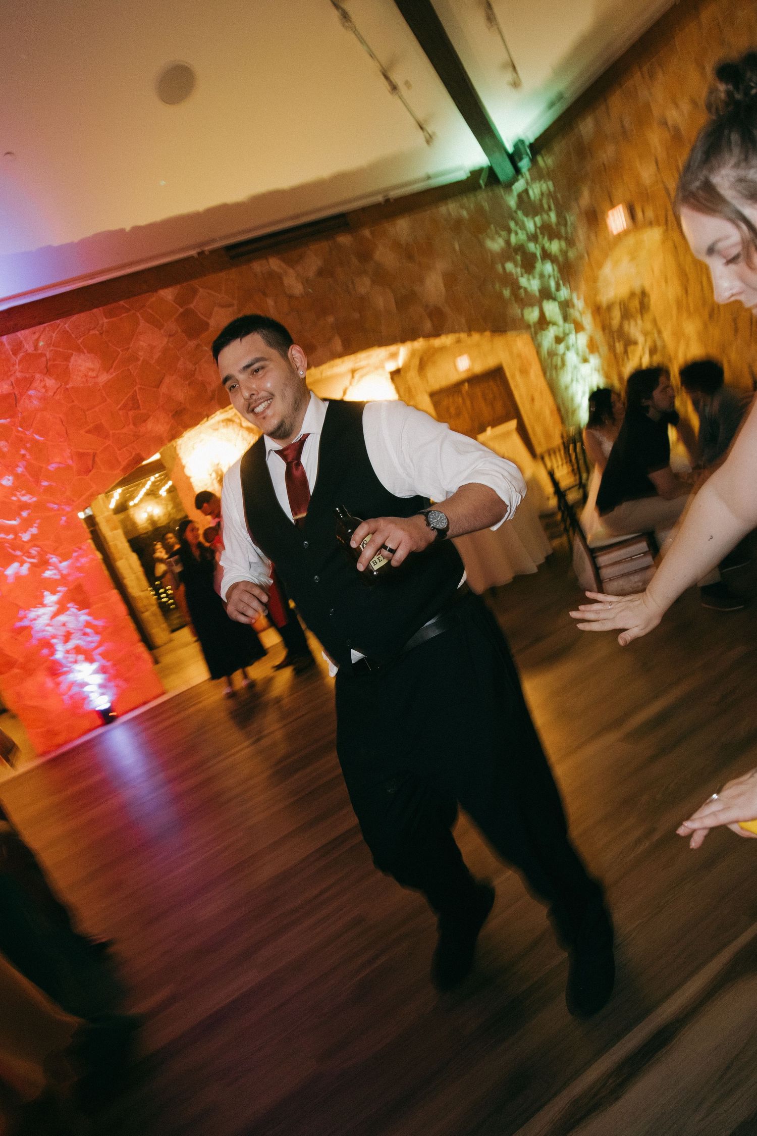 Smiling groomsman in vest dancing energetically at a wedding reception.