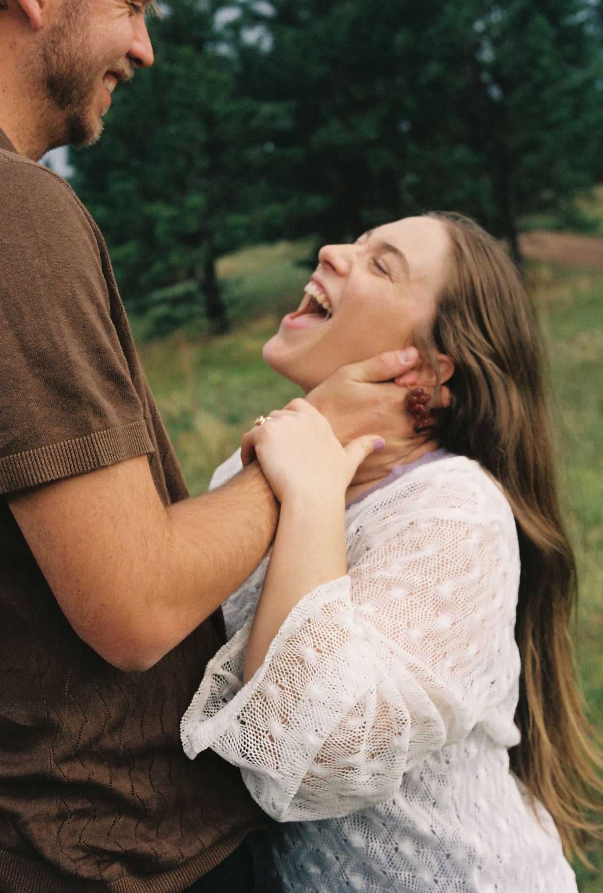 Woman laughing joyfully while holding a mans face during a playful outdoor moment together.