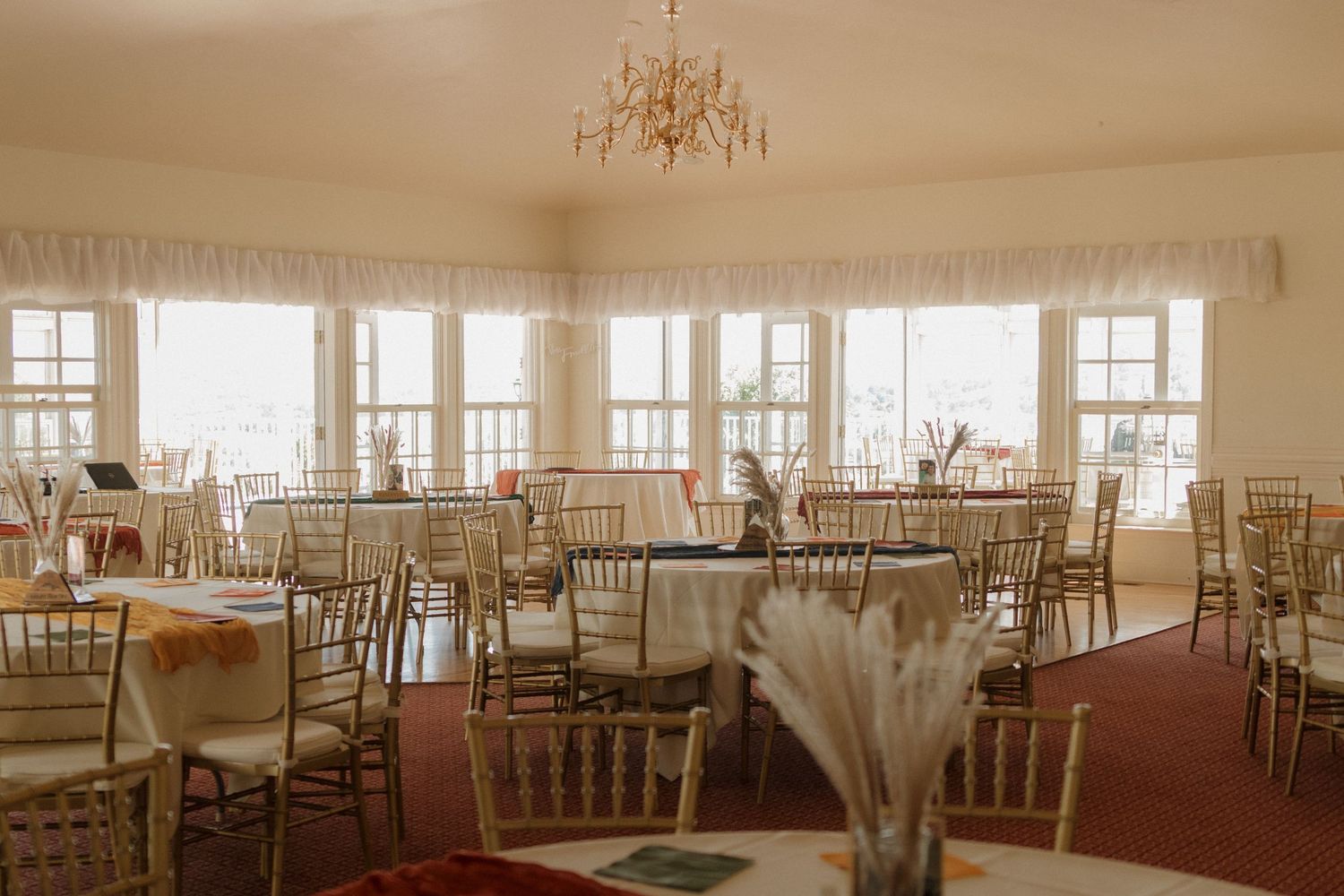 Elegant reception hall set with white linens and gold chiavari chairs under crystal chandeliers.