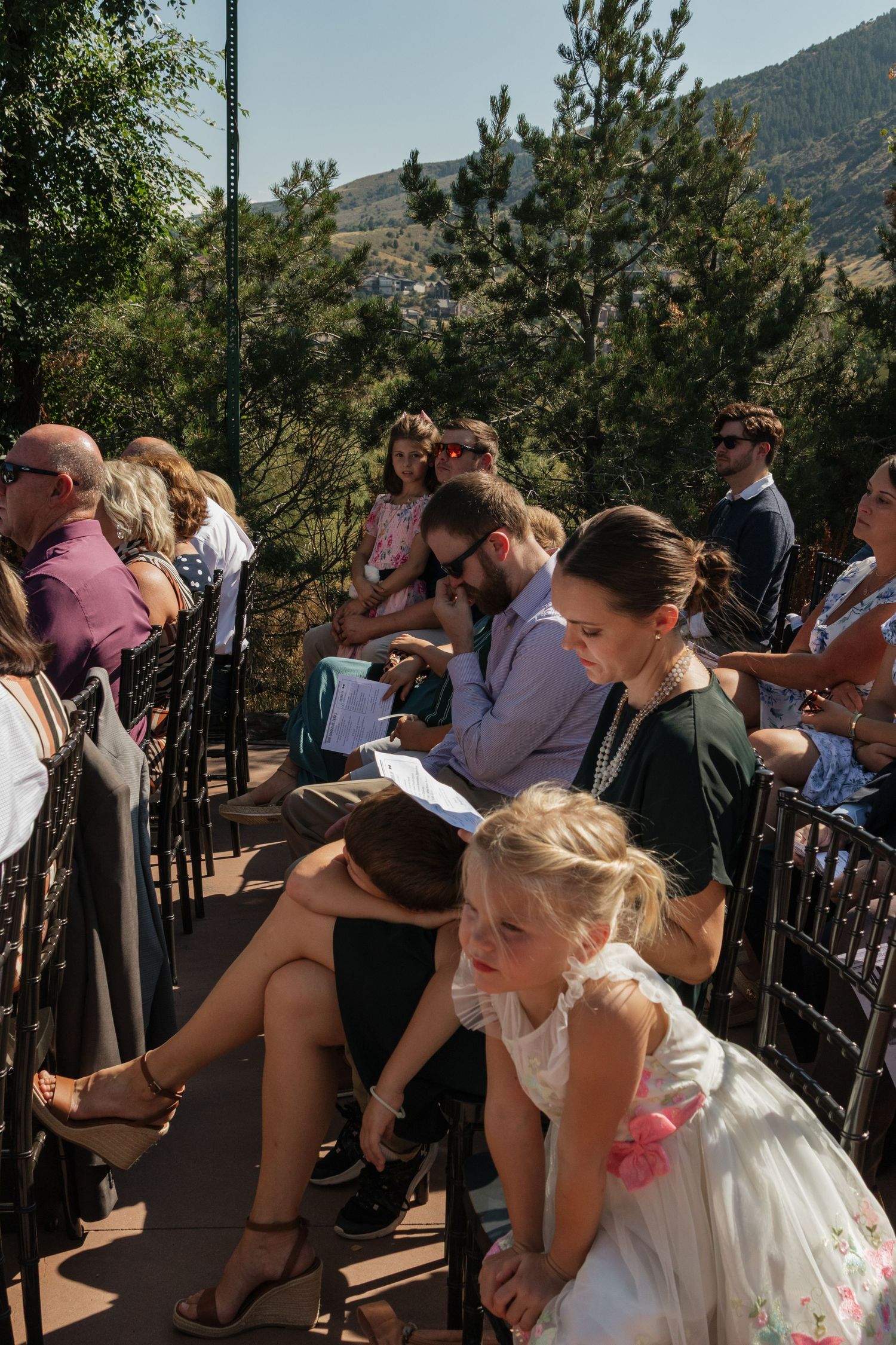 Wedding guests stand together on an outdoor terrace with mountain views in the background.
