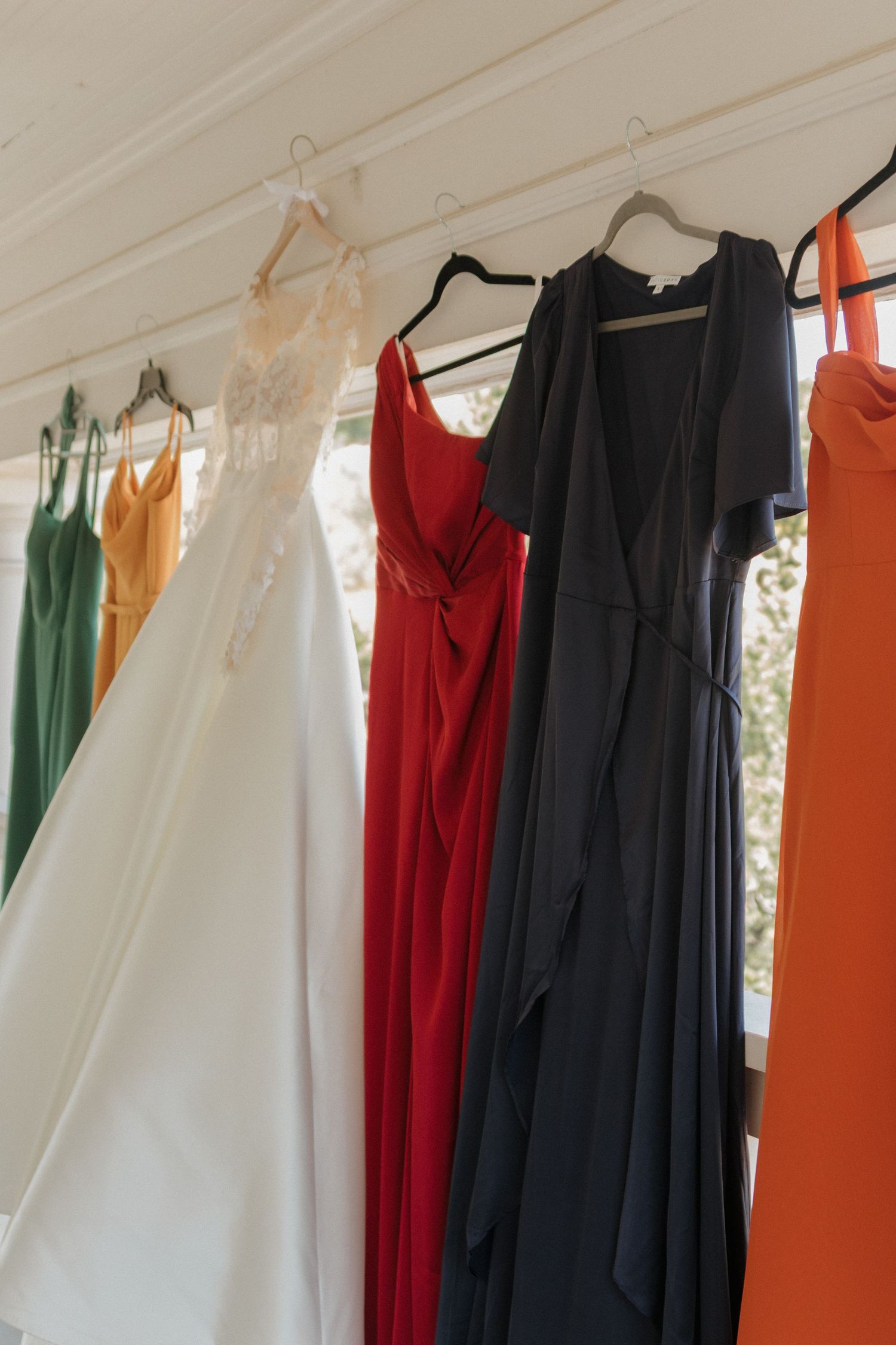 Colorful formal dresses hanging on a rack including red, green, orange and white gowns.