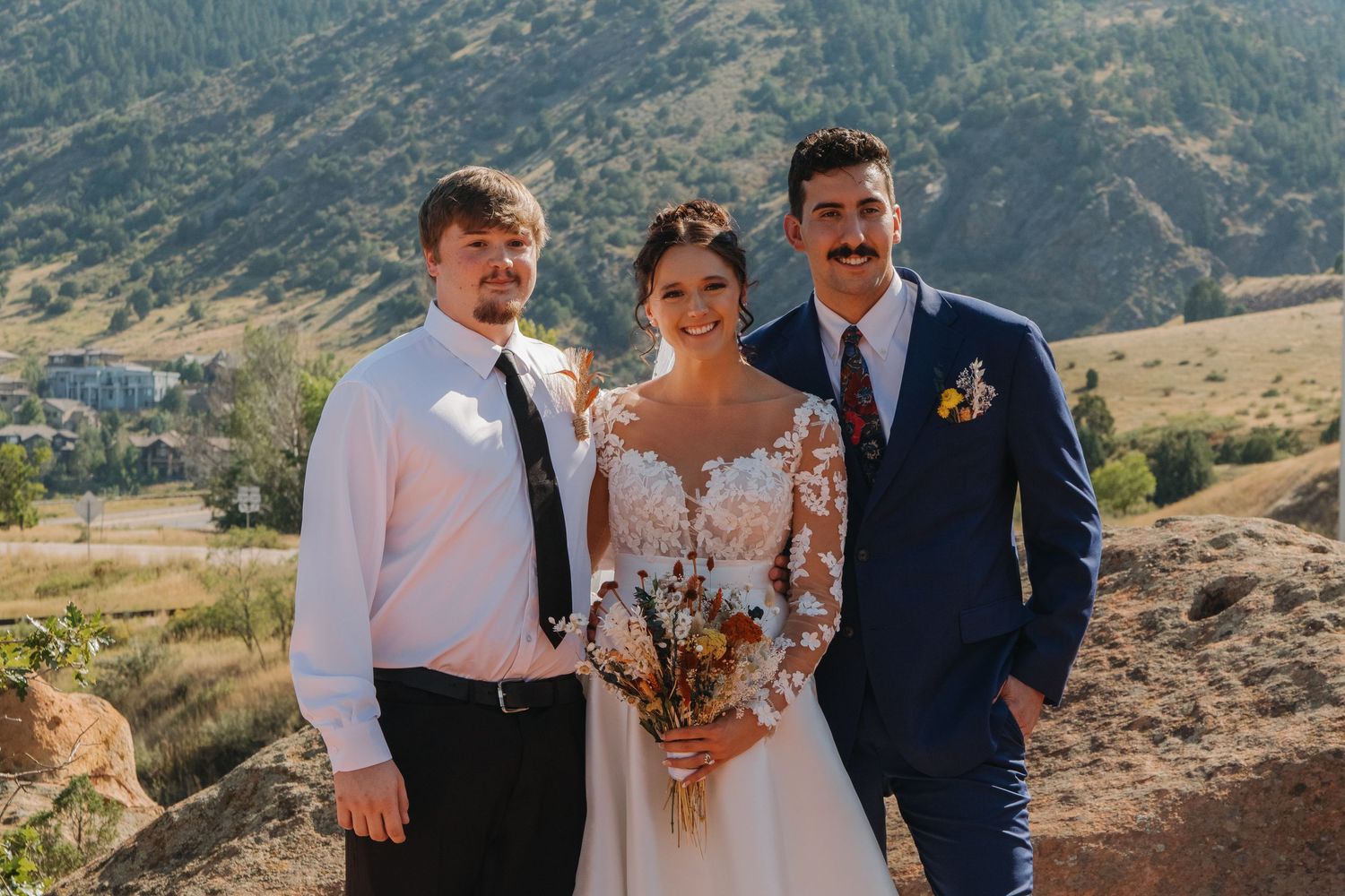 Wedding party poses against dramatic mountain landscape on sunny day.
