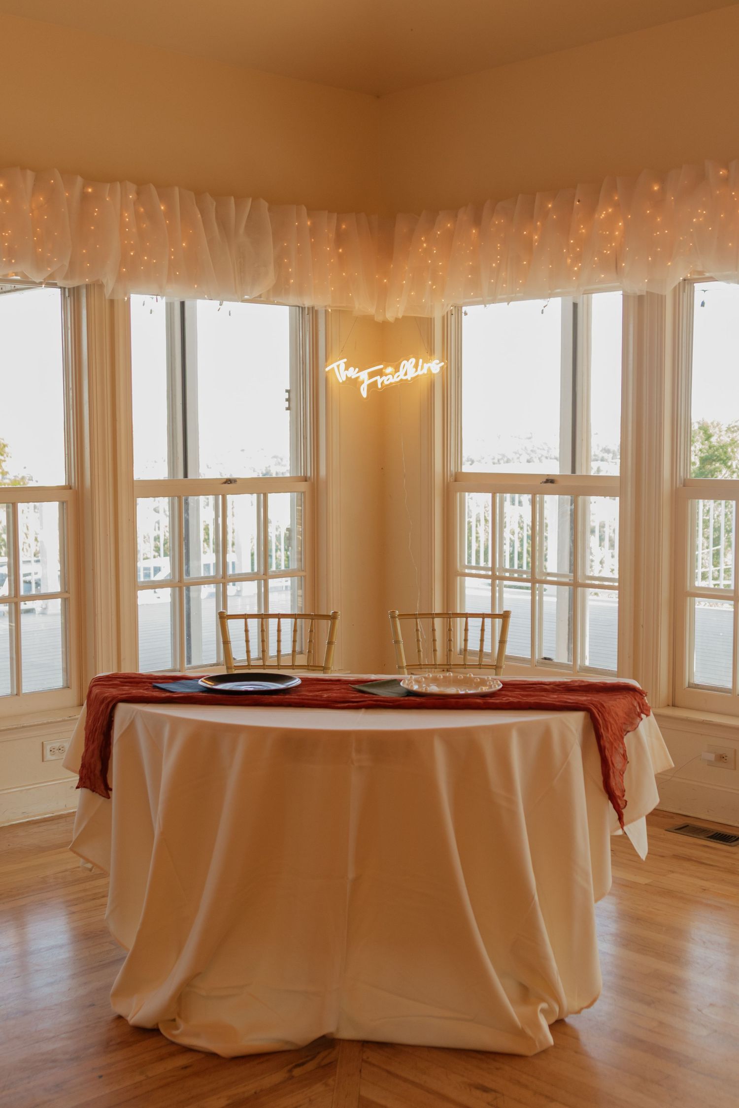 Empty wedding reception room with round tables covered in white linens and large windows.