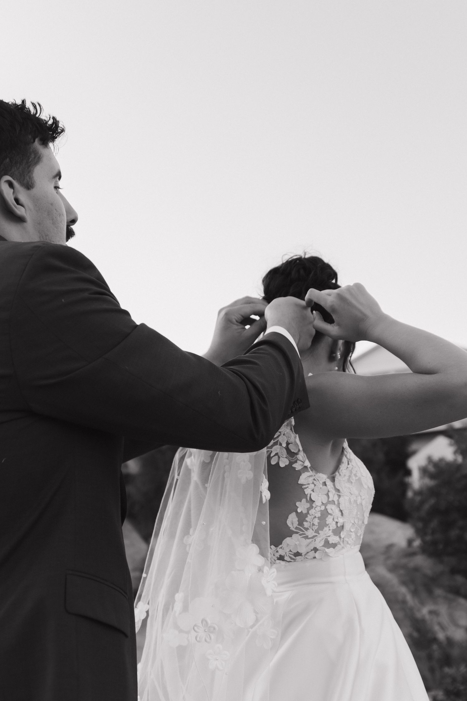 Black and white image showing wedding dress being adjusted outdoors.