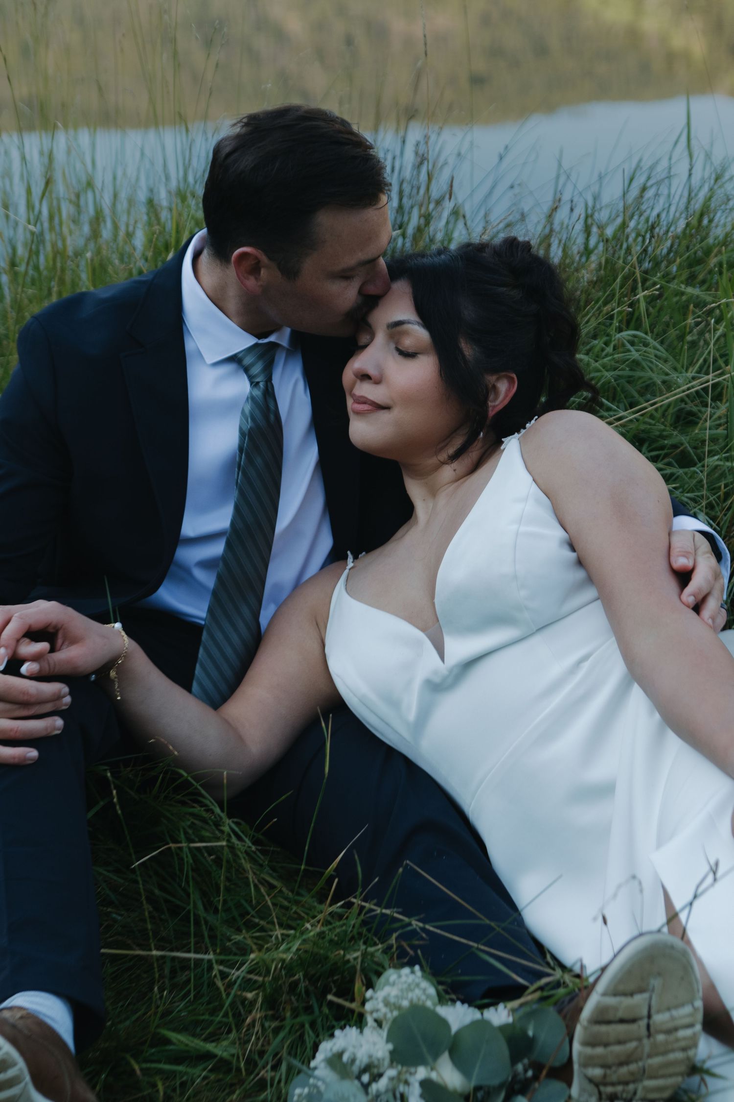 Couple shares romantic moment in tall grass by mountain lake.