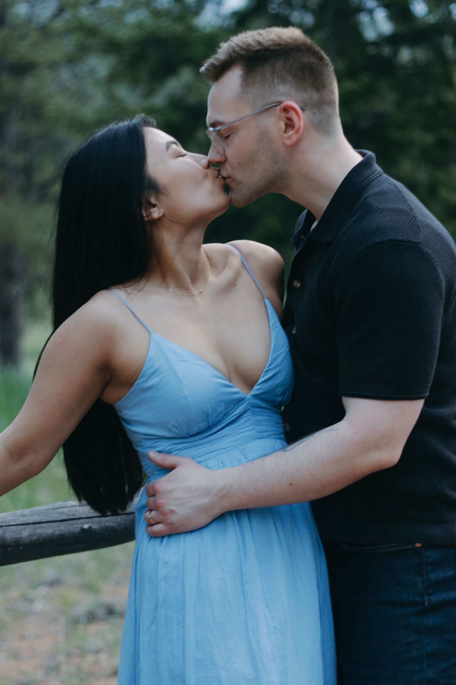 A couple shares a tender kiss against a natural forest backdrop.