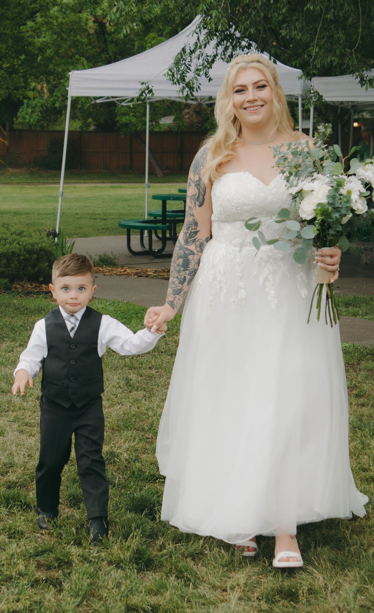 Wedding party poses for casual photos on grass with white flowers and formal attire.