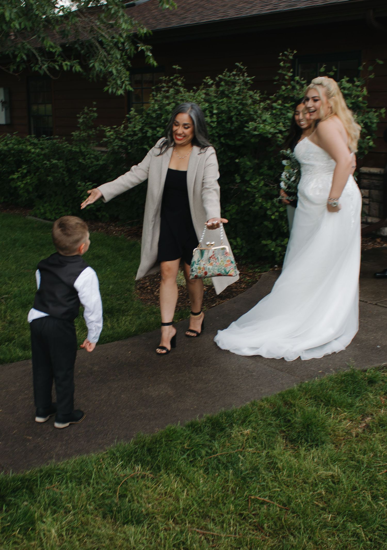 A bride in a white gown interacts with a young ring bearer on a garden path.