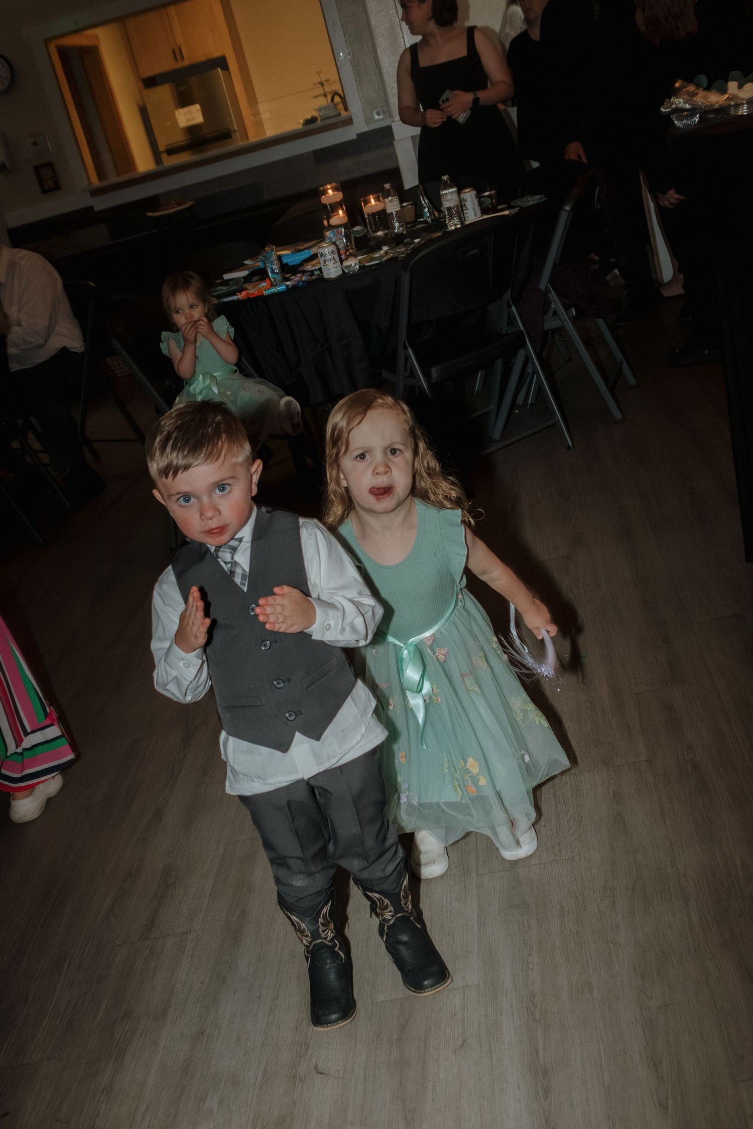 Two young children in formal attire dance together at a wedding reception.
